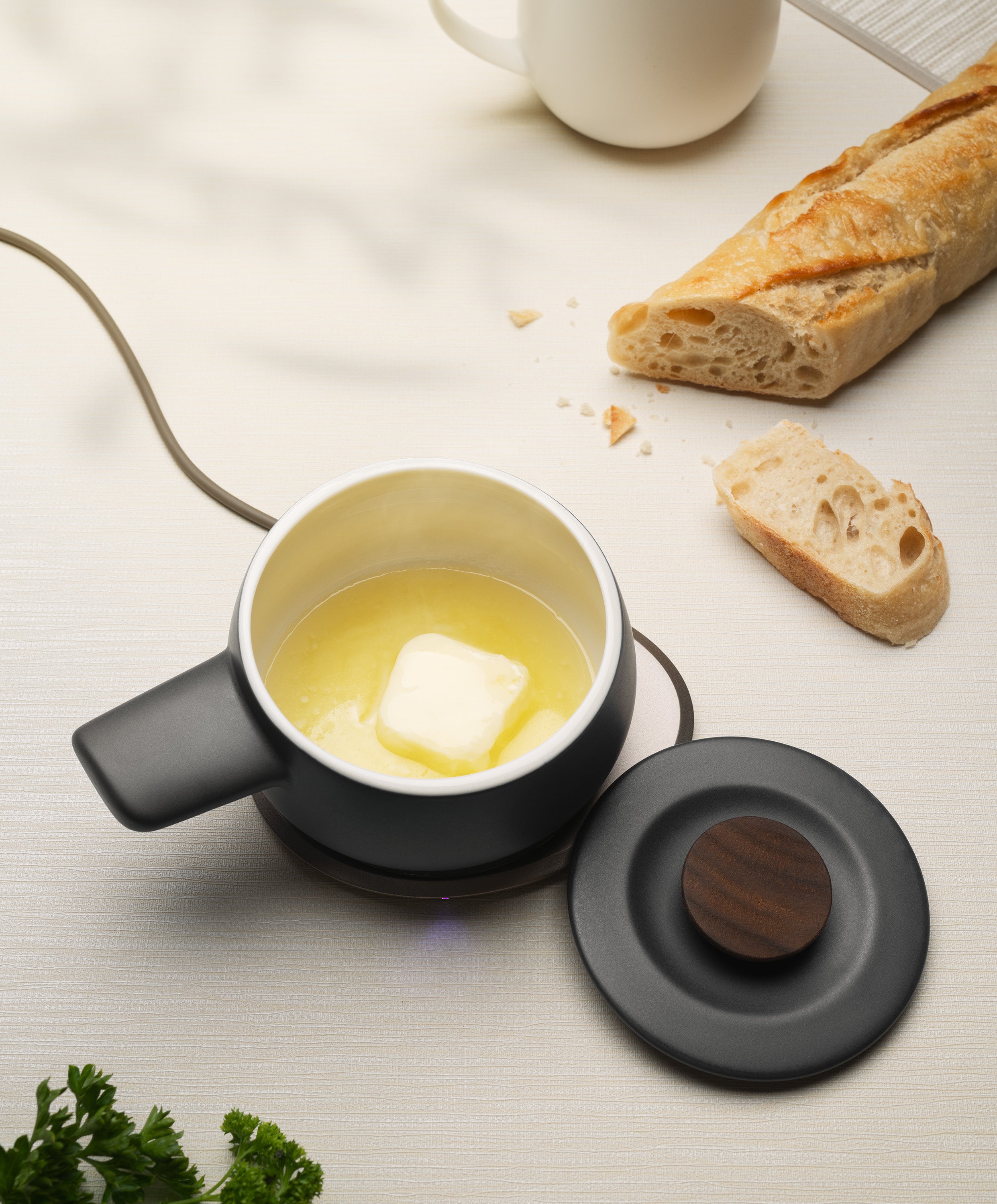 Fondi self-heating ceramic fondue 7.6 fl oz / 225 mL in Inkstone Black with butter melting on OHOM Pad 3, lid on side and bread nearby