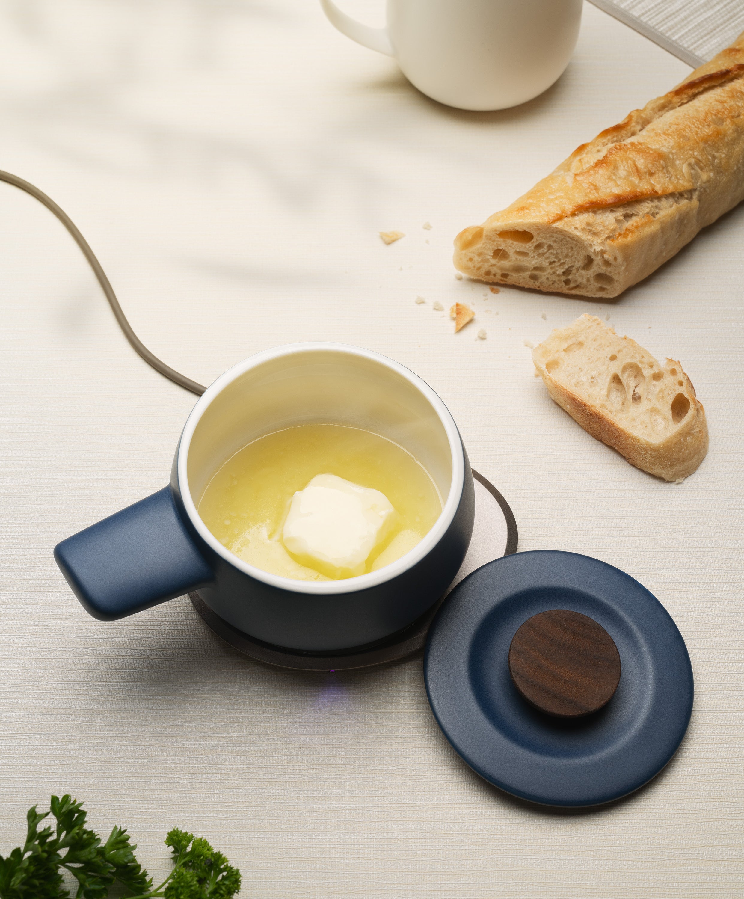 Fondi self-heating ceramic fondue 7.6 fl oz / 225 mL in Deep Navy with butter melting on OHOM Pad 3, lid on side and bread nearby