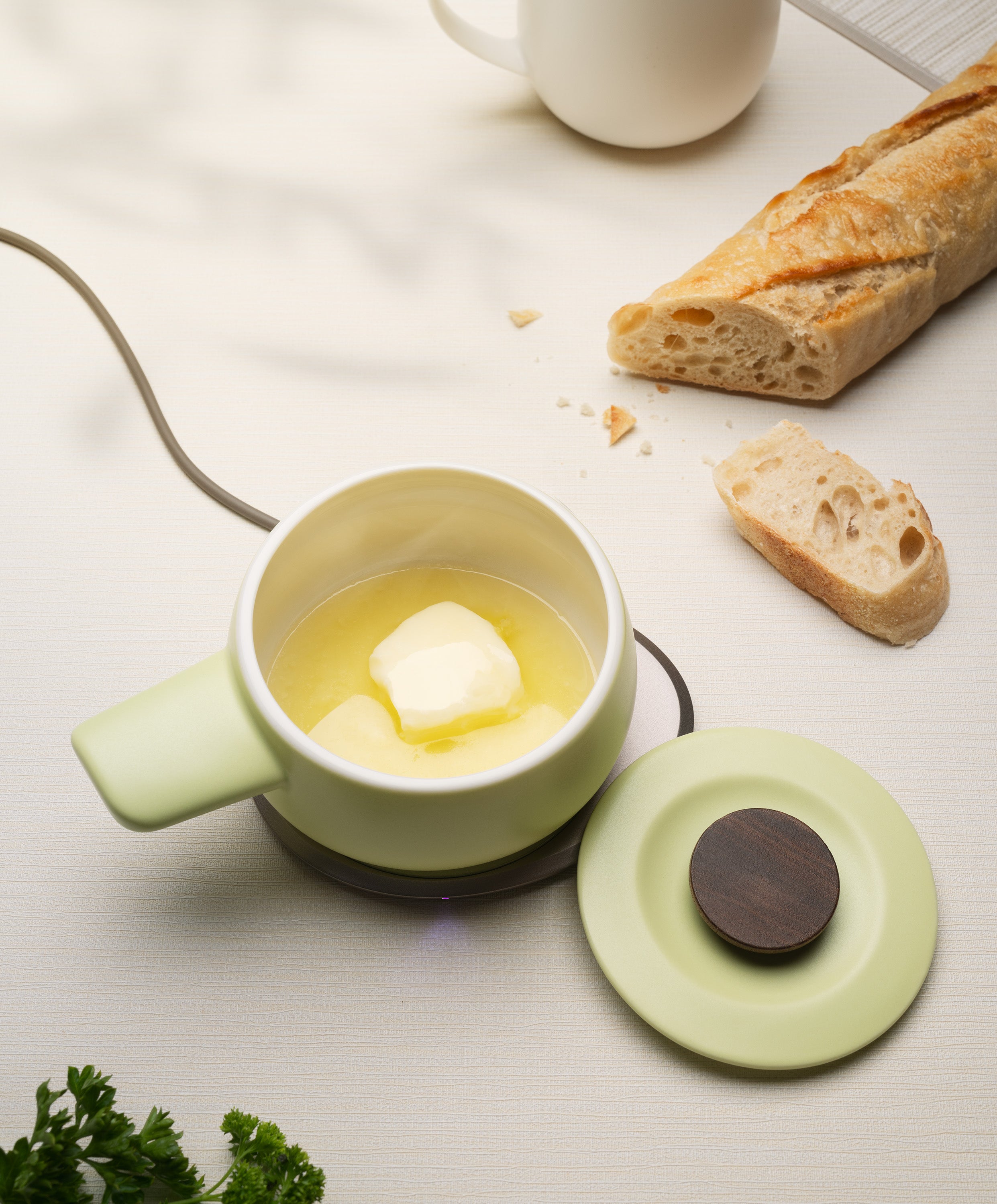 Fondi self-heating ceramic fondue 7.6 fl oz / 225 mL in Verde Green with butter melting on OHOM Pad 3, lid on side and bread nearby