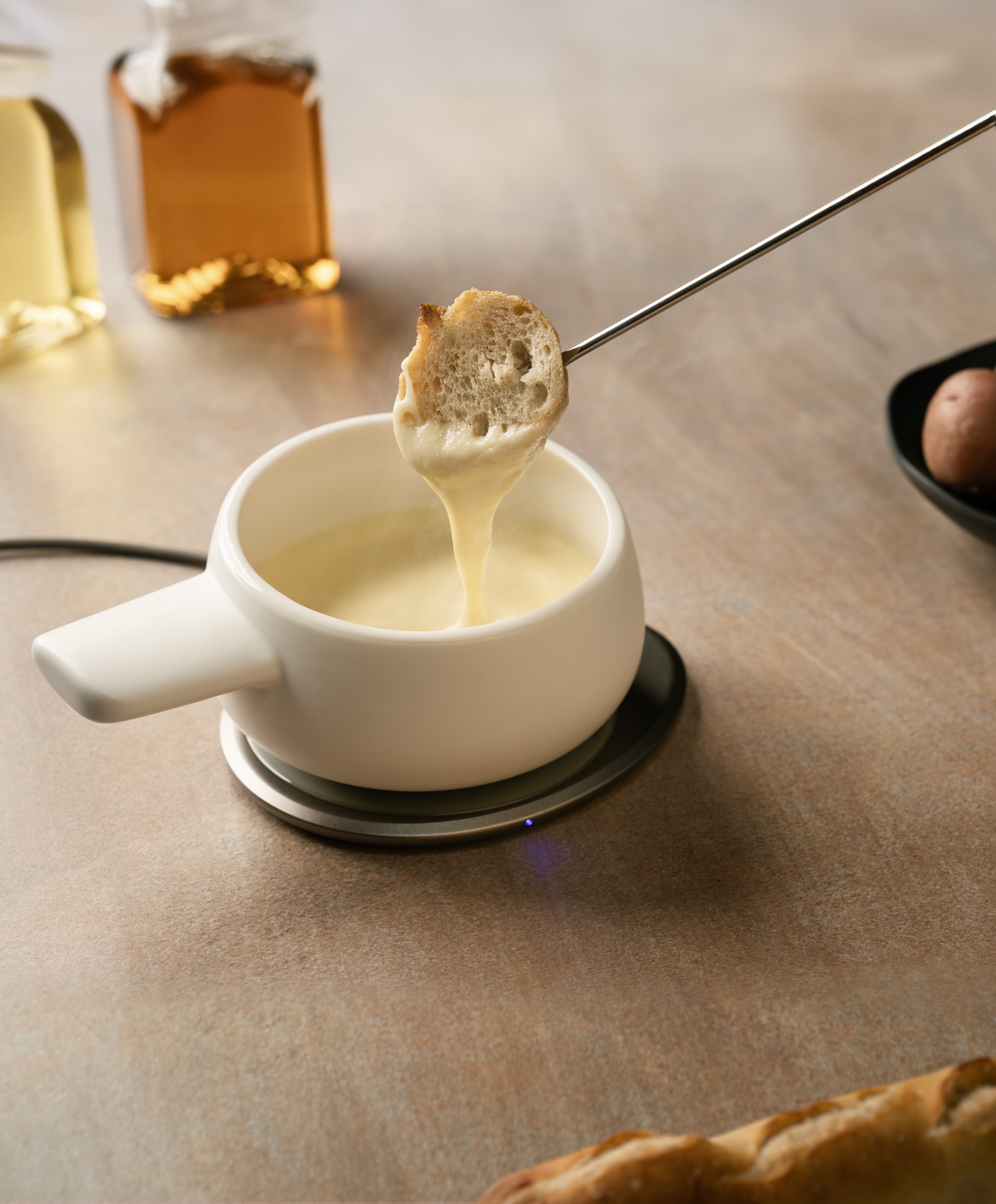Melted cheese in the Fondi Self-heating Fondue Set 7.6 fl oz on the OHOM Pad with a piece of bread dipping in