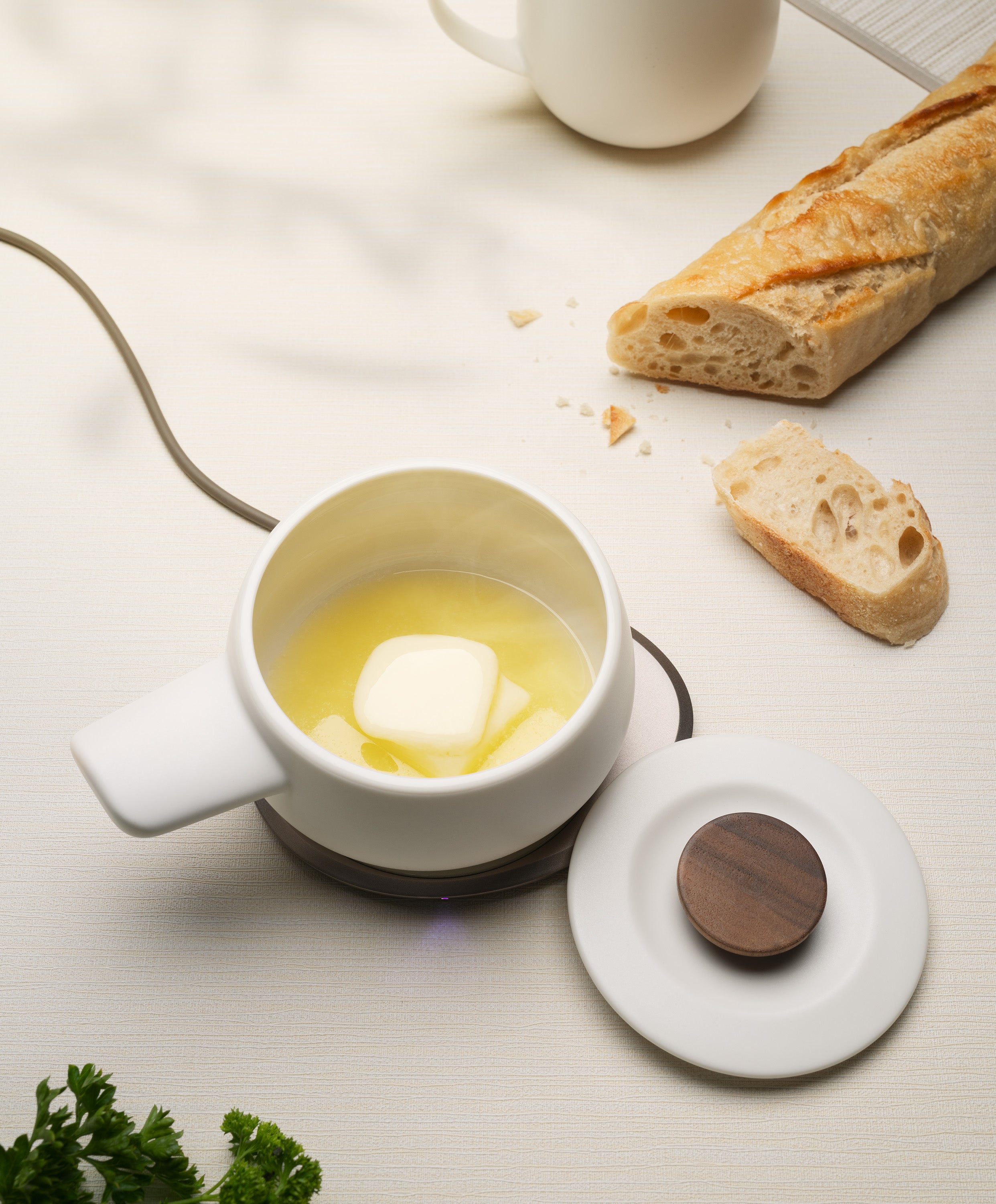 Cheese melting in the Fondi Self-heating Fondue Set 7.6 fl oz on the OHOM Pad with the lid, sliced baguette, and whole baguette beside it