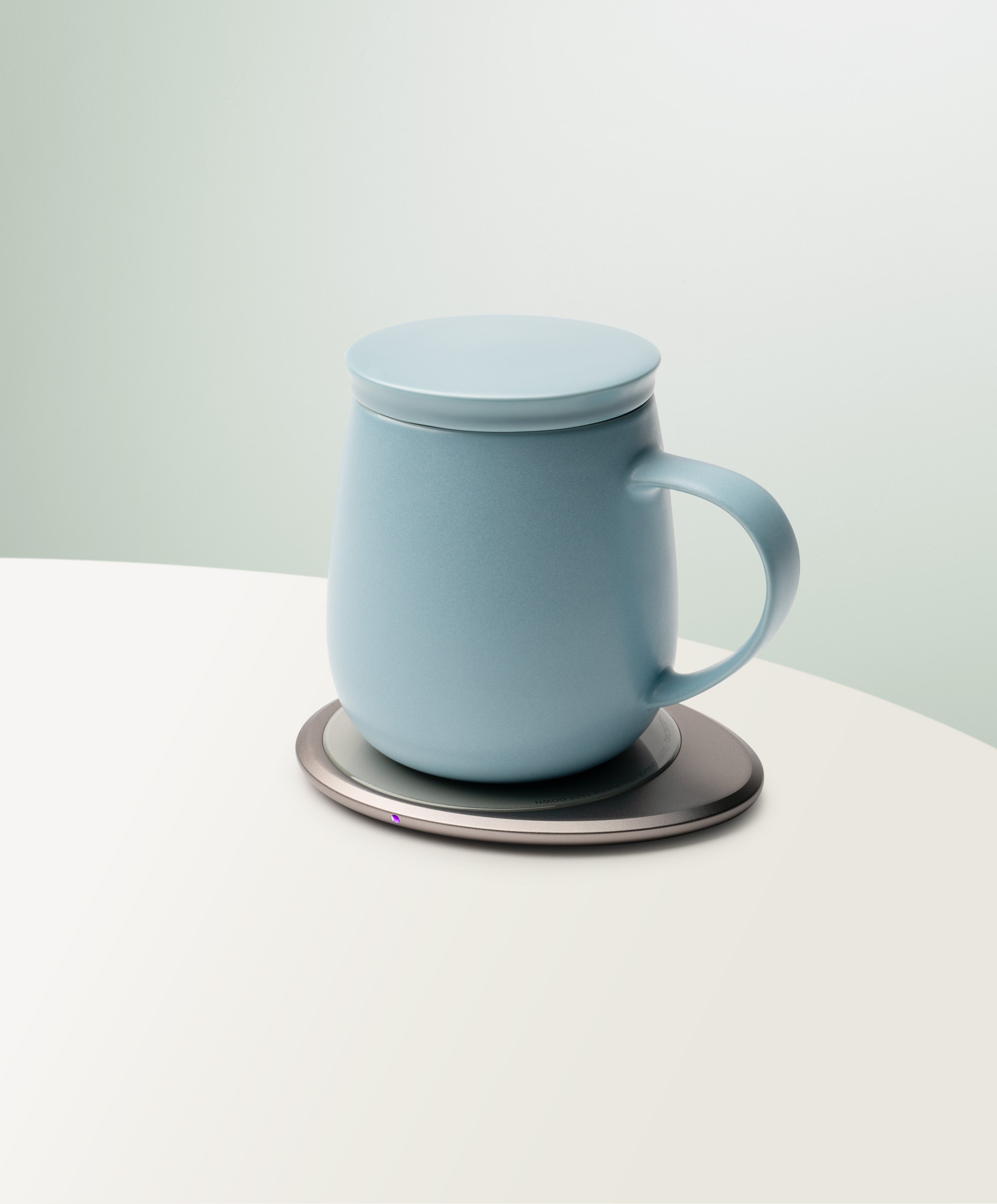 Ui 3 Self-Heating Ceramic Mug 12 fl oz / 355 mL in Moonmist Blue with lid angled top-side view on OHOM Charging Pad 3