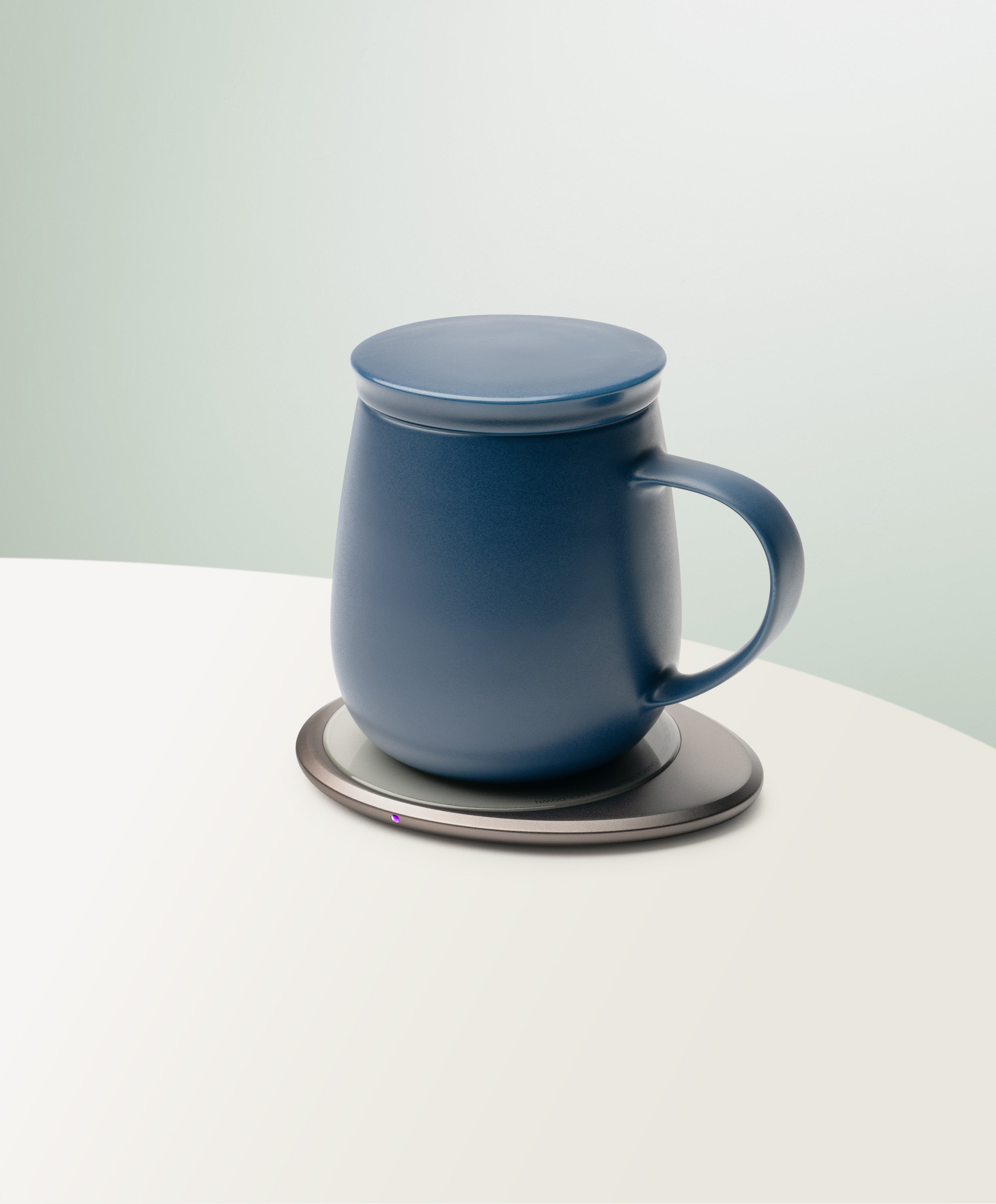 Ui 3 Self-Heating Ceramic Mug 12 fl oz / 355 mL in Deep Navy with lid angled top-side view on OHOM Charging Pad 3