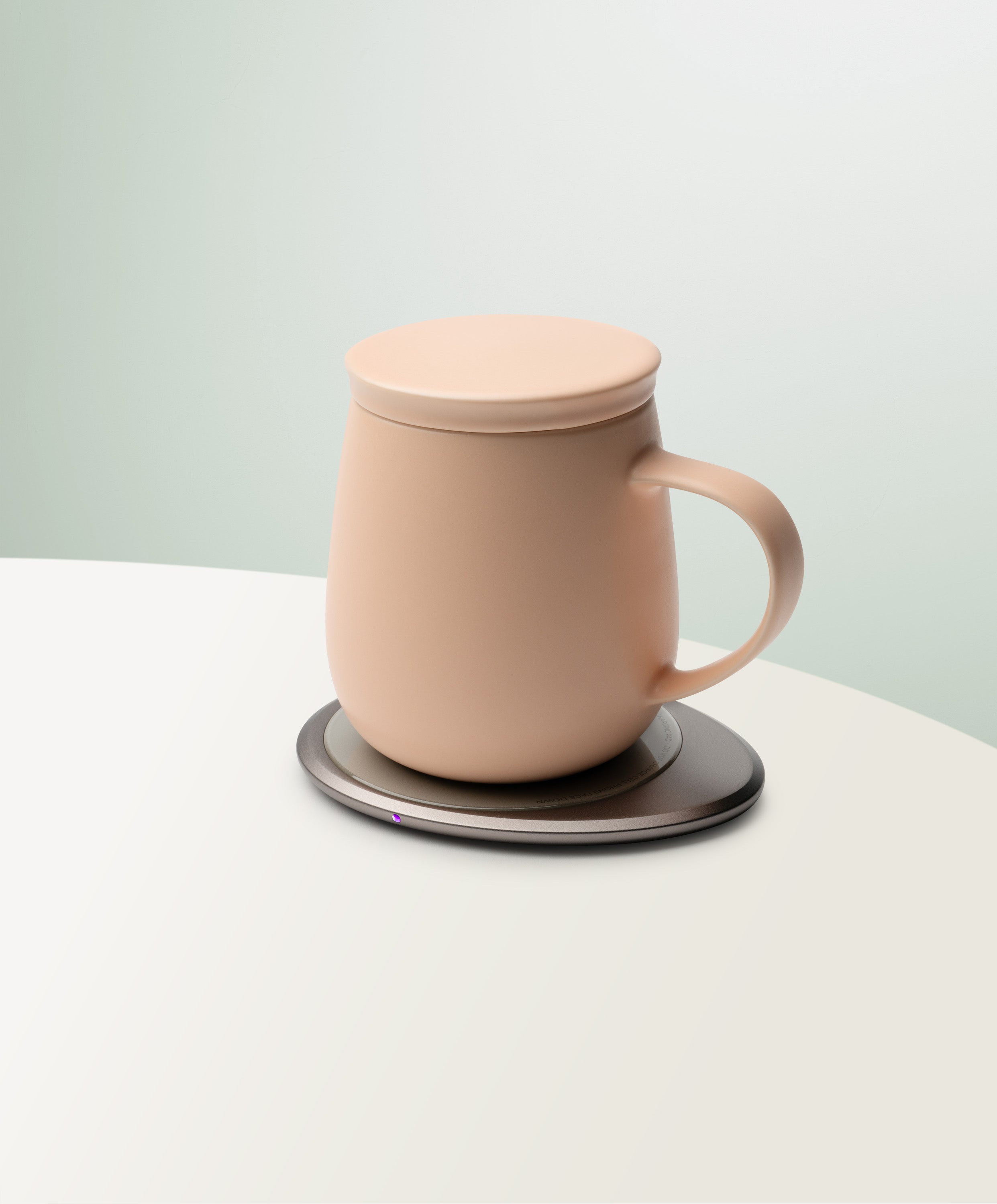 Ui 3 Self-Heating Ceramic Mug 12 fl oz / 355 mL in Rosy Apricot with lid angled top-side view on OHOM Charging Pad 3