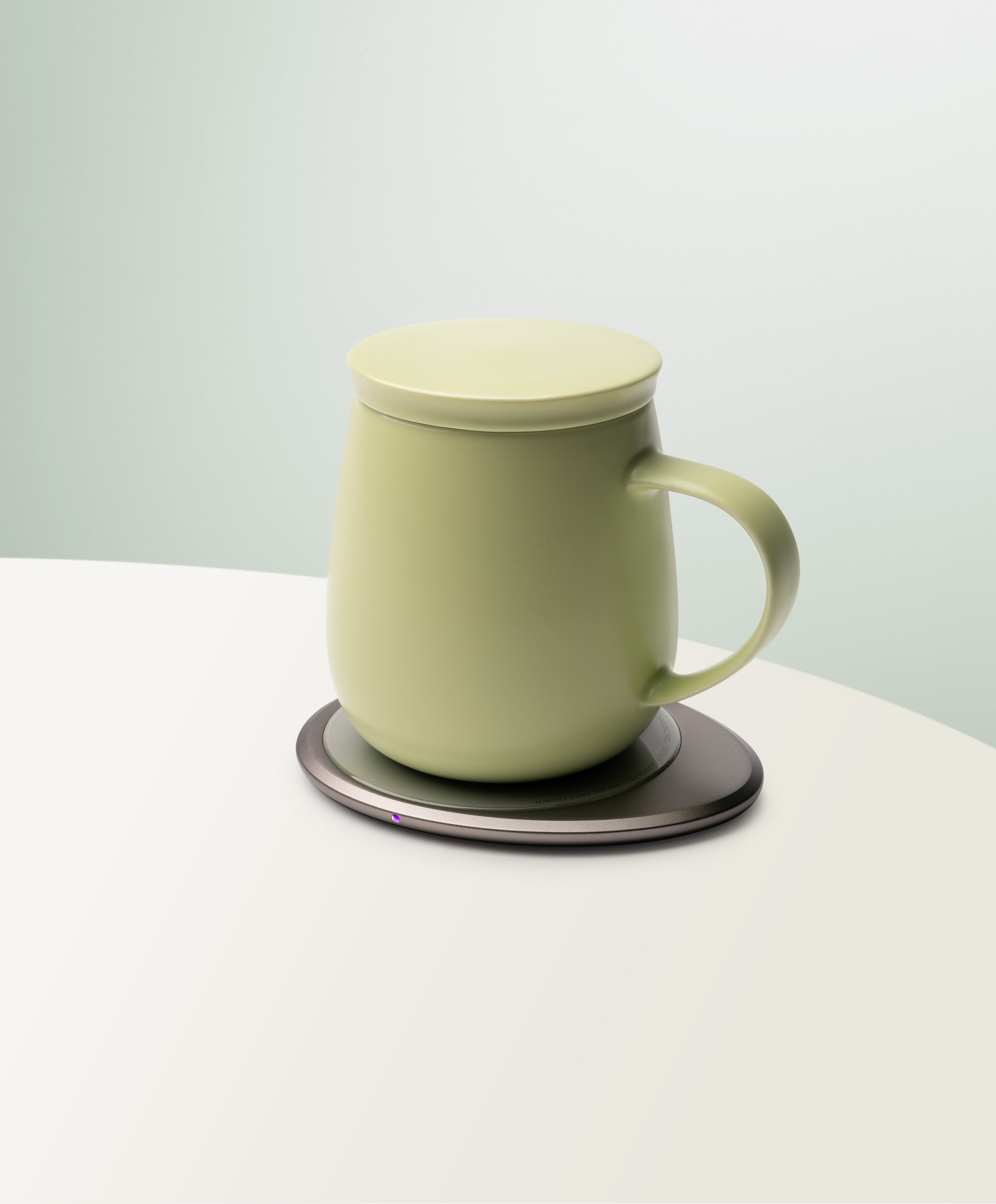 Ui 3 Self-Heating Ceramic Mug 12 fl oz / 355 mL in Verde Green with lid angled top-side view on OHOM Charging Pad 3