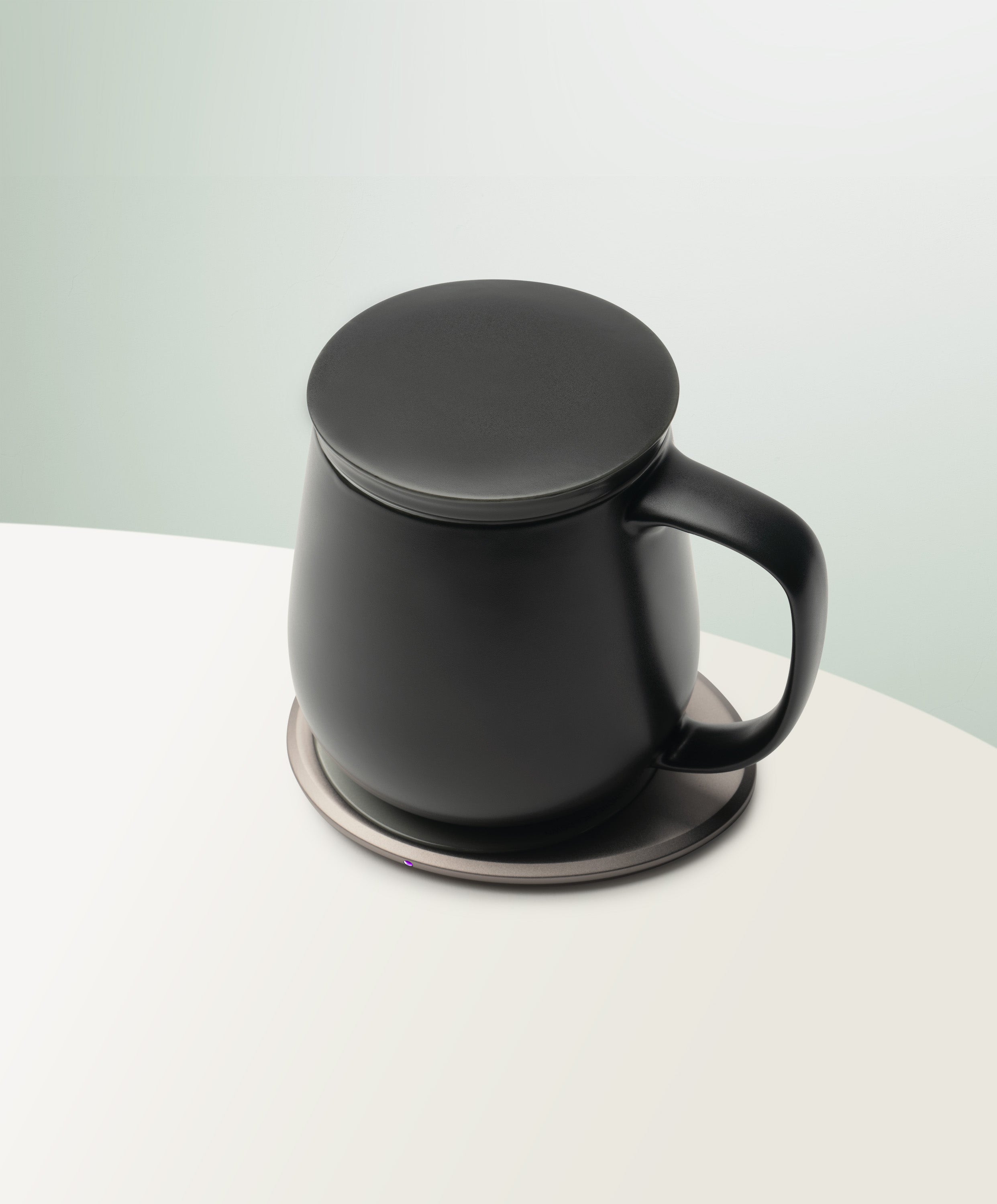 Ui+ Self-Heating Ceramic Mug 18 fl oz / 532 mL in Inkstone Black with lid angled top-side view on OHOM Charging Pad 3