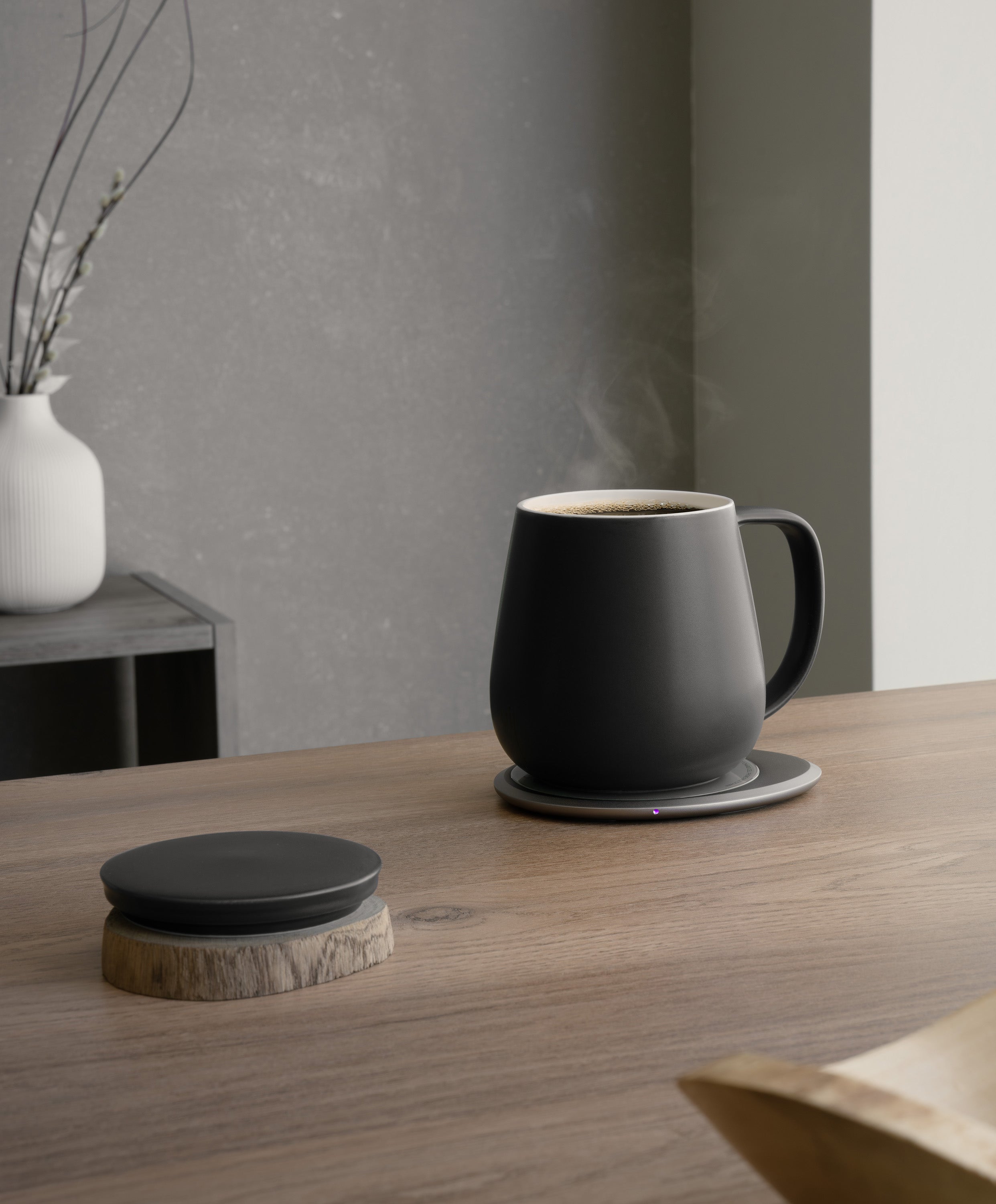 Ui+ self-heating ceramic mug set 18 fl oz / 532 mL in Inkstone Black charging on OHOM Pad 3, lid placed on wooden coaster