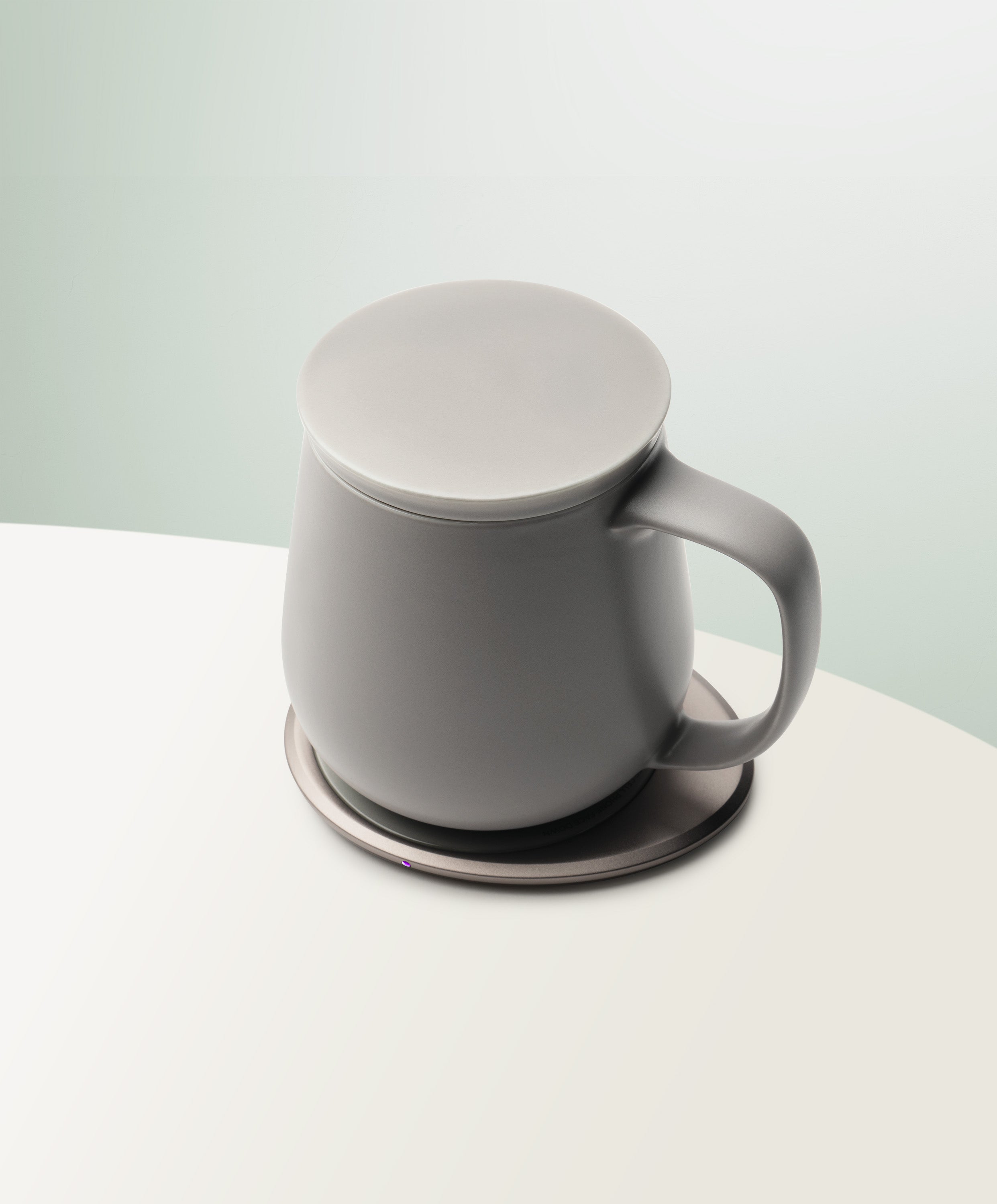 Ui+ Self-Heating Ceramic Mug 12 fl oz / 355 mL in Soft Gray with lid angled top-side view on OHOM Charging Pad 3
