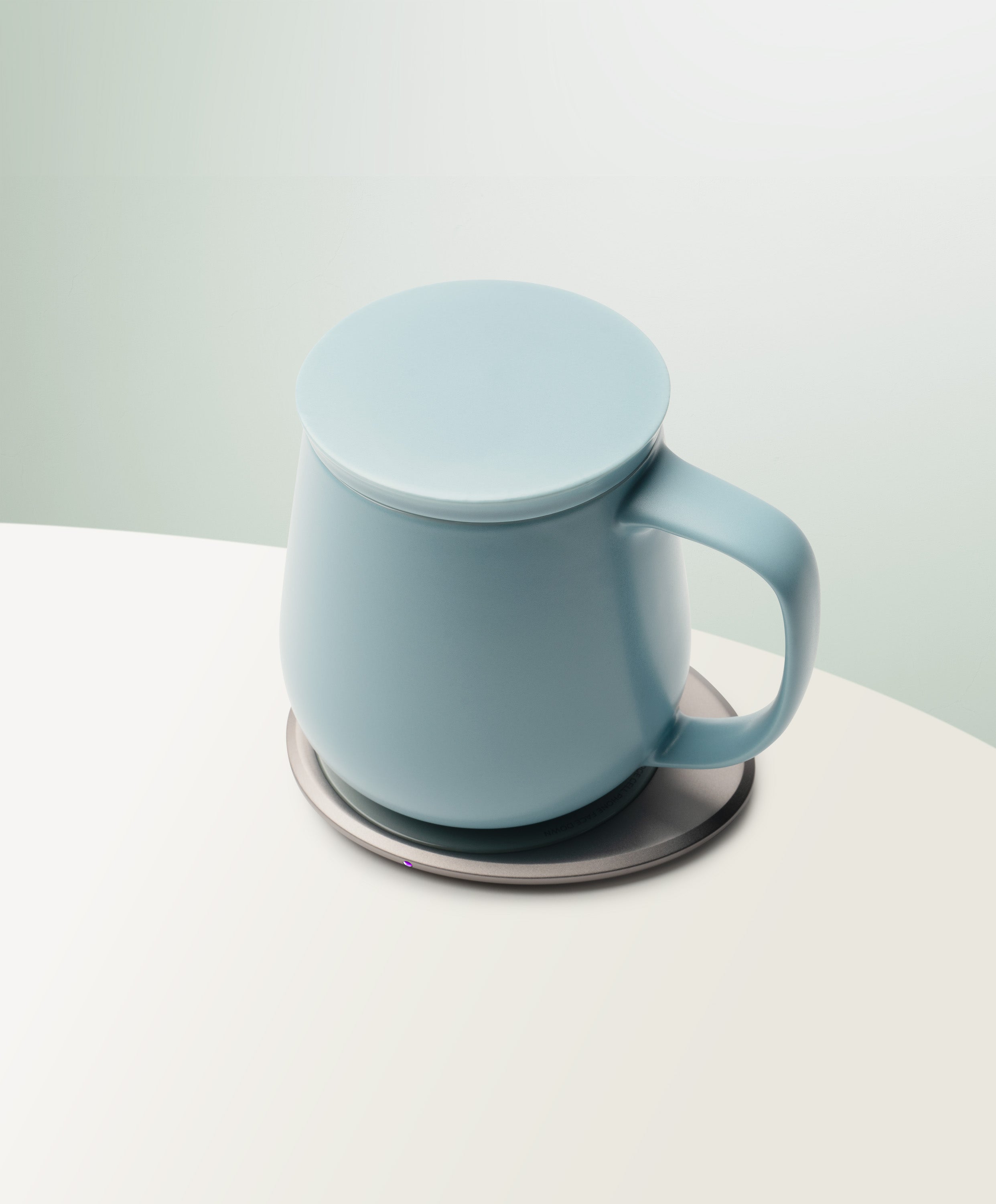 Ui+ Self-Heating Ceramic Mug 18 fl oz / 532 mL in Moonmist Blue with lid angled top-side view on OHOM Charging Pad 3