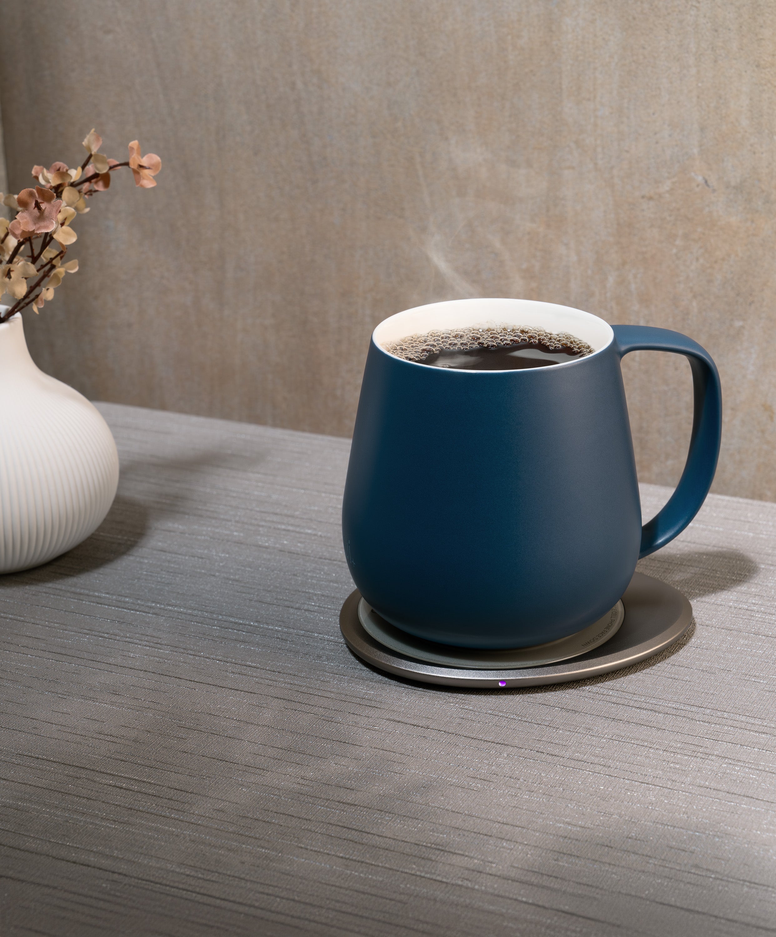 Ui+ self-heating ceramic mug set 18 fl oz / 532 mL in Deep Navy charging on OHOM Pad 3, filled with hot coffee and steam rising