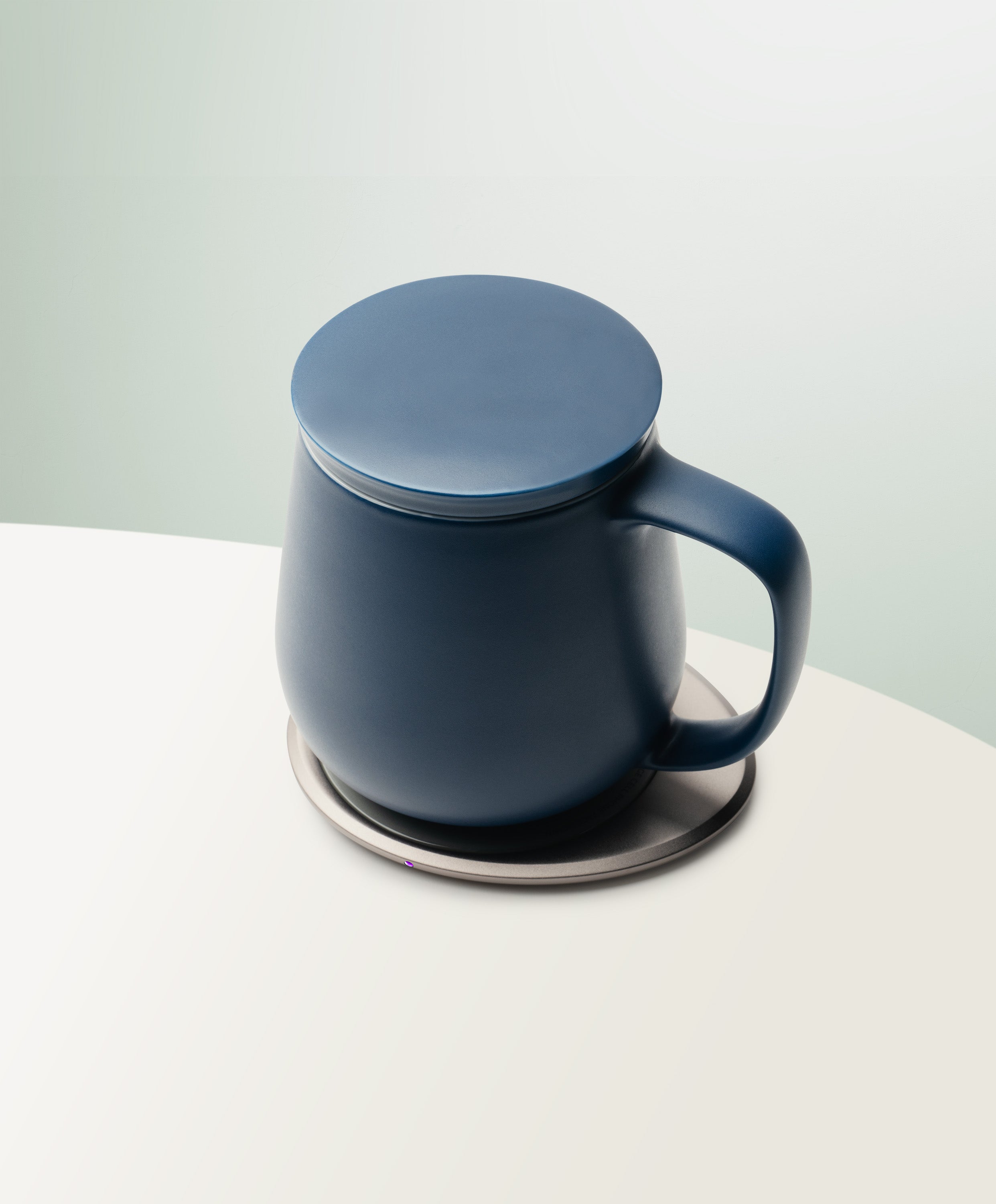 Ui+ Self-Heating Ceramic Mug 18 fl oz / 532 mL in Deep Navy with lid angled top-side view on OHOM Charging Pad 3