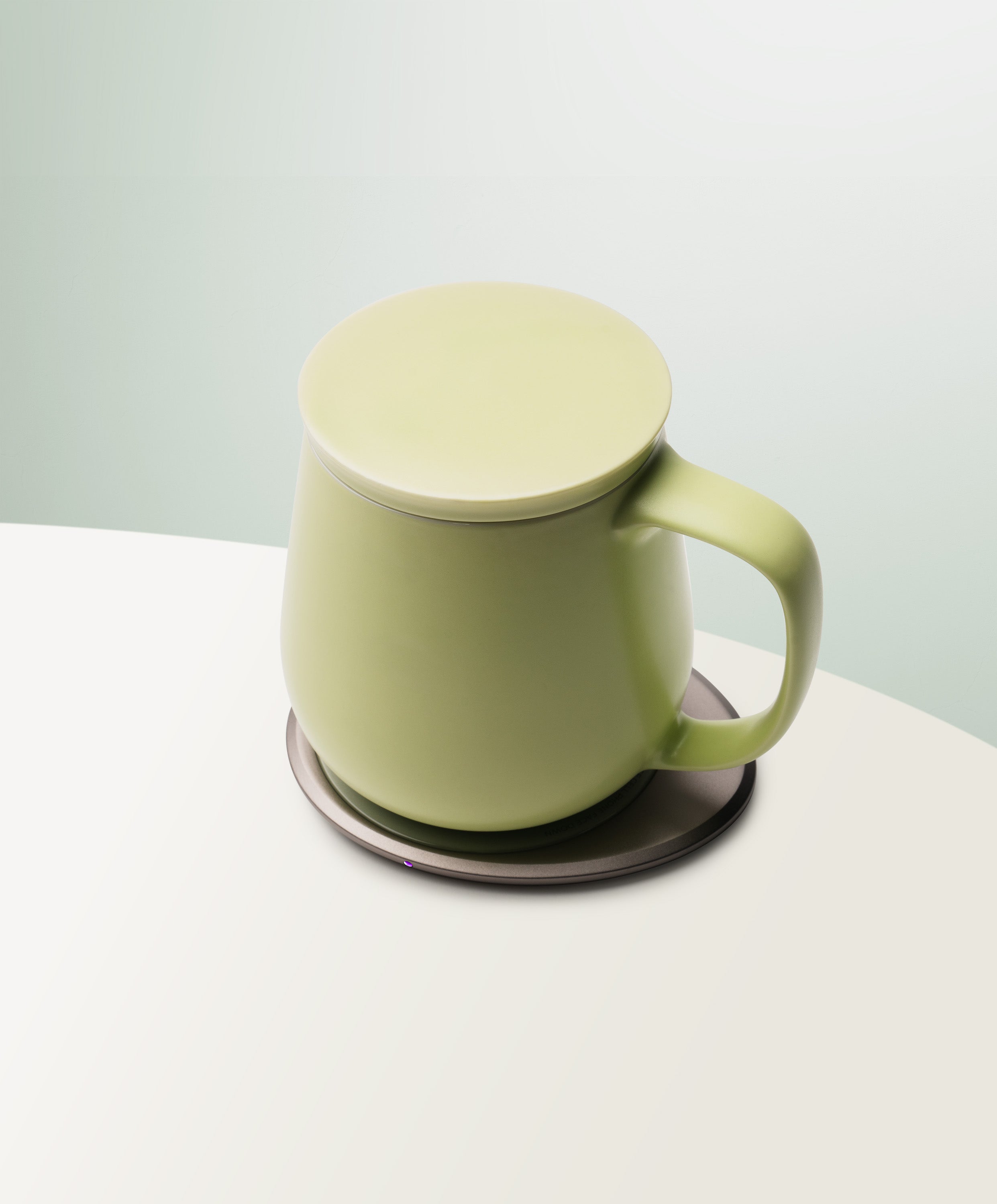 Ui+ Self-Heating Ceramic Mug 18 fl oz / 532 mL in Verde Green with lid angled top-side view on OHOM Charging Pad 3