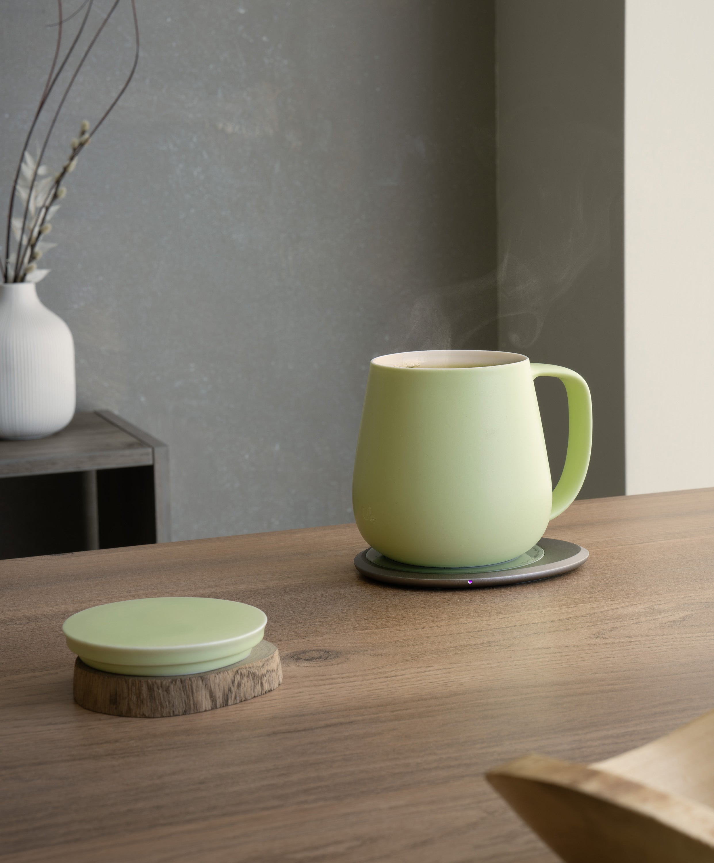 Ui+ self-heating ceramic mug set 18 fl oz / 532 mL in Verde Green charging on OHOM Pad 3, lid placed on wooden coaster