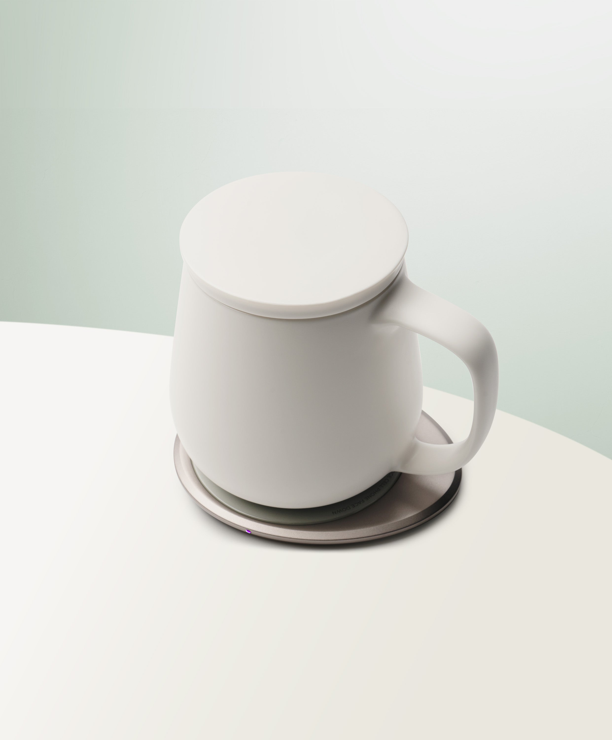 Ui+ Self-Heating Ceramic Mug 18 fl oz / 532 mL in Jasmine White with lid angled top-side view on OHOM Charging Pad 3