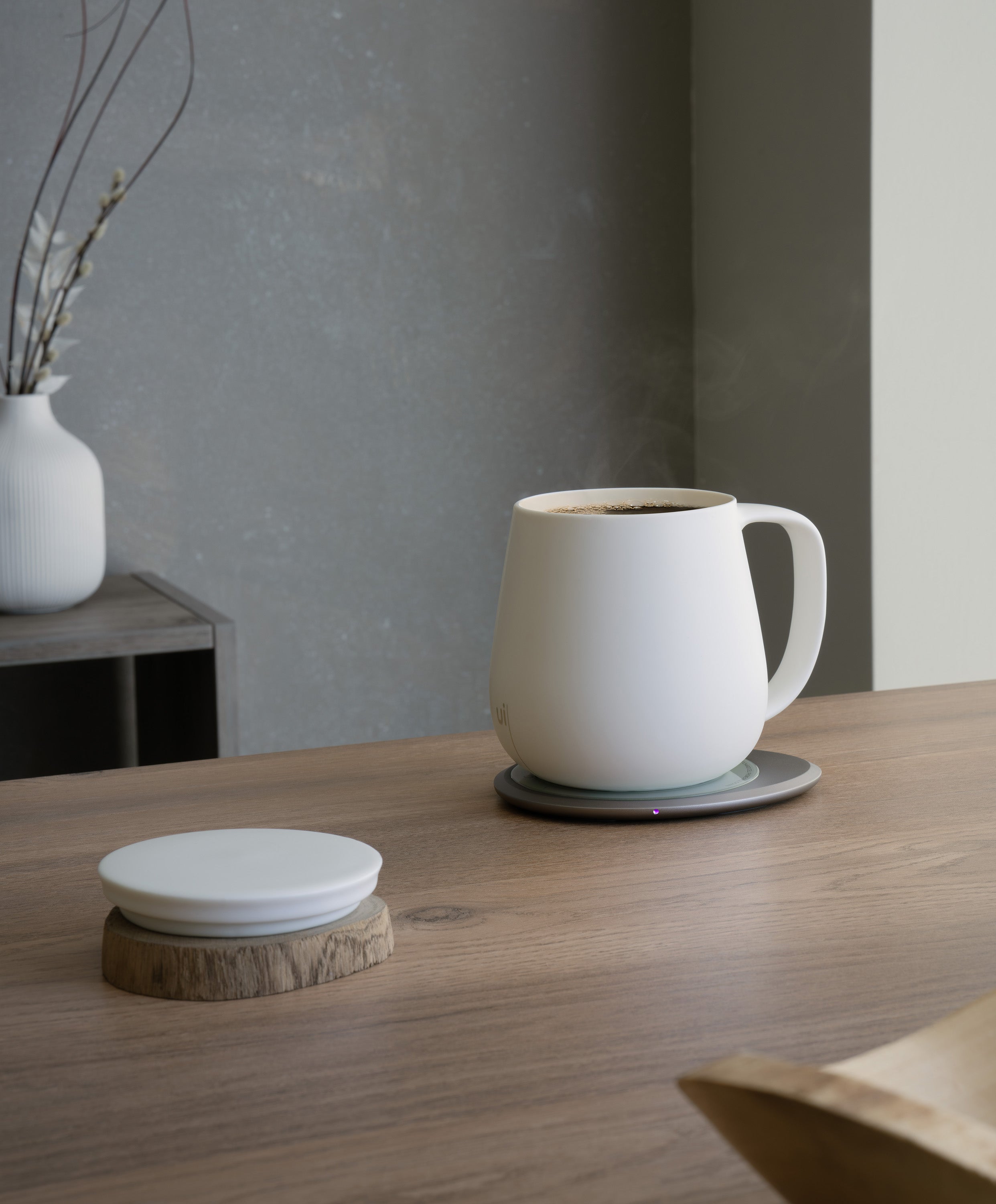 Ui+ self-heating ceramic mug set 18 fl oz / 532 mL in Jasmine White charging on OHOM Pad 3, lid placed on wooden coaster