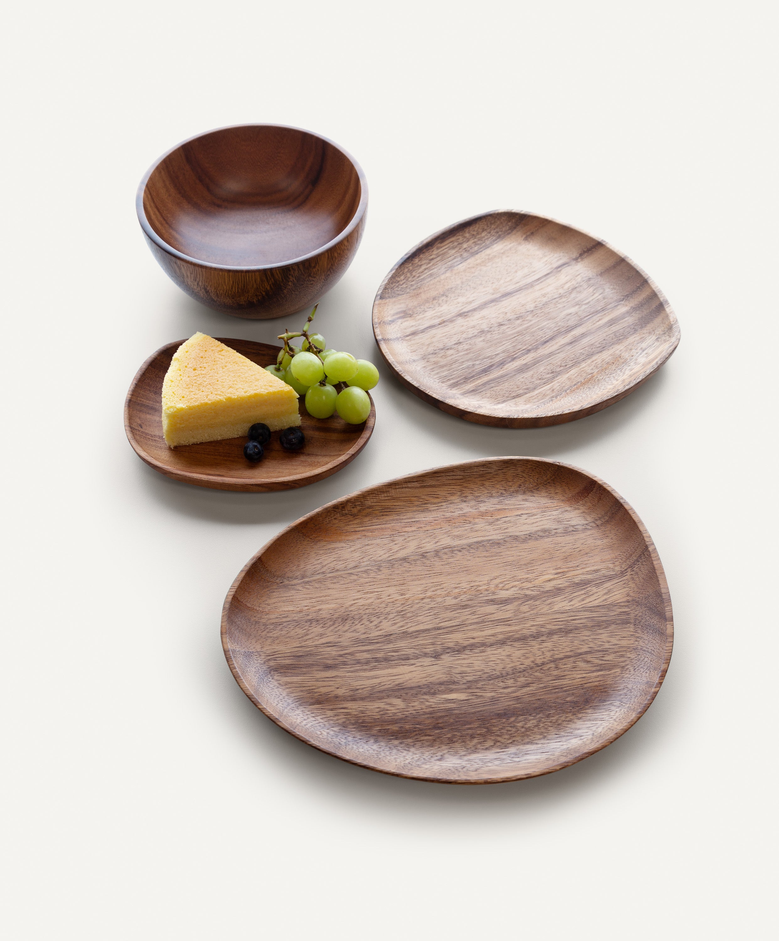 Foree wooden dinnerware set handcrafted from solid Acacia wood with large, medium, and small plates and salad bowl, small plate holding cake, grapes, and blueberries