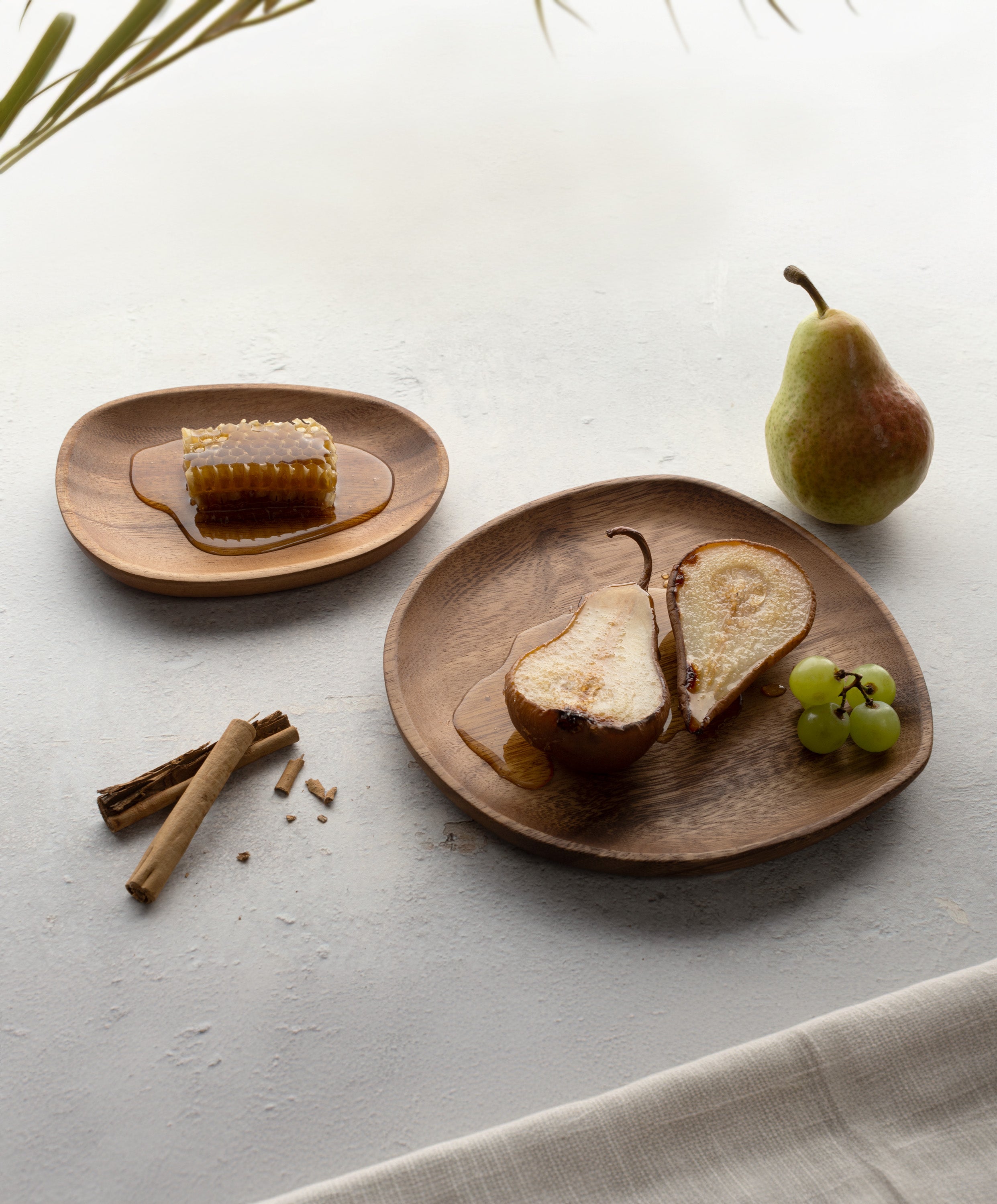 Foree wooden dinnerware set handcrafted from solid Acacia wood with large plate holding sliced pear and grapes, medium plate with honey, and cinnamon stick and pear on the side