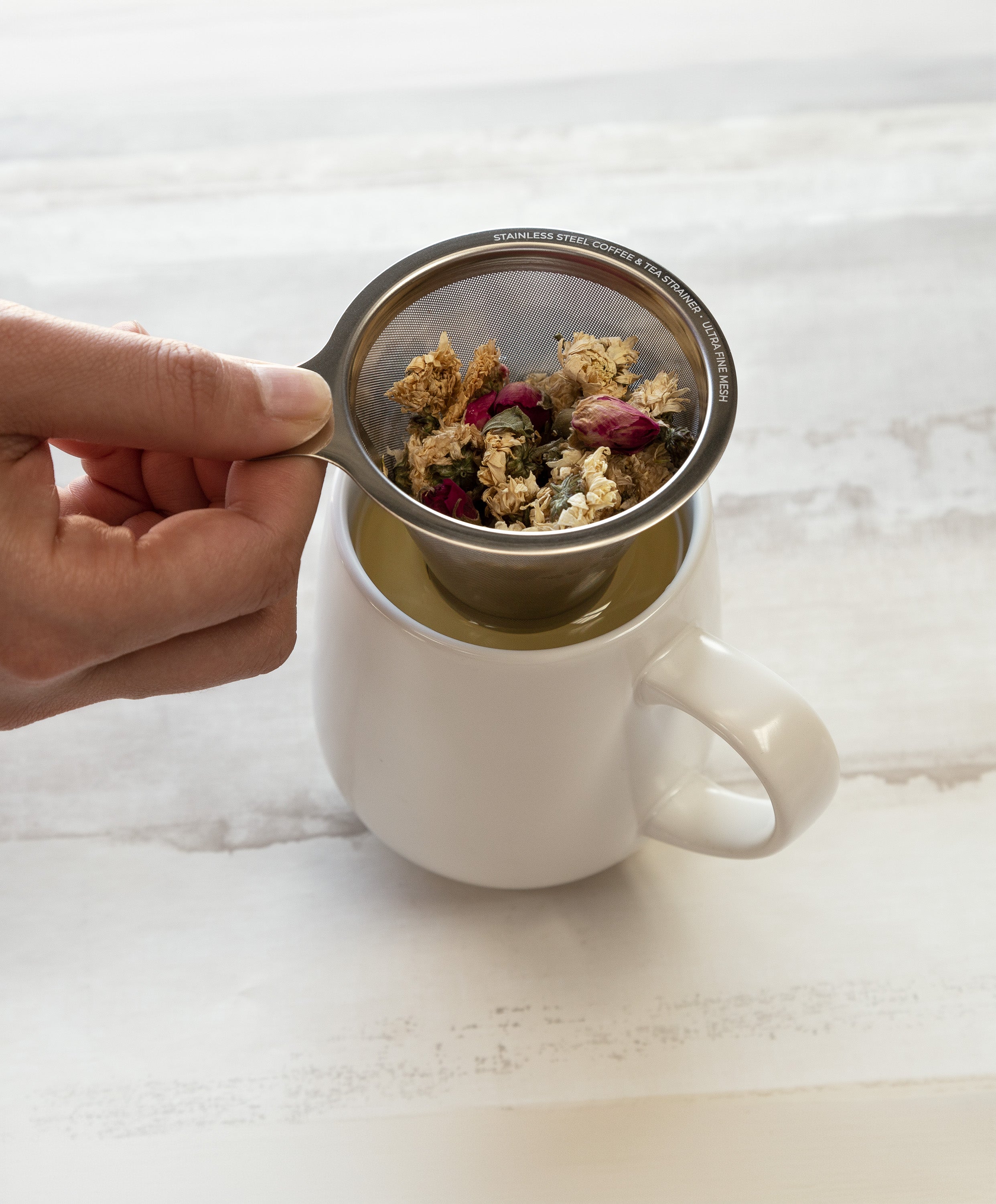 Ui large stainless steel strainer being removed from Ui 2 / Ui 3 self-heating ceramic mug 12 fl oz, showing brewed tea inside