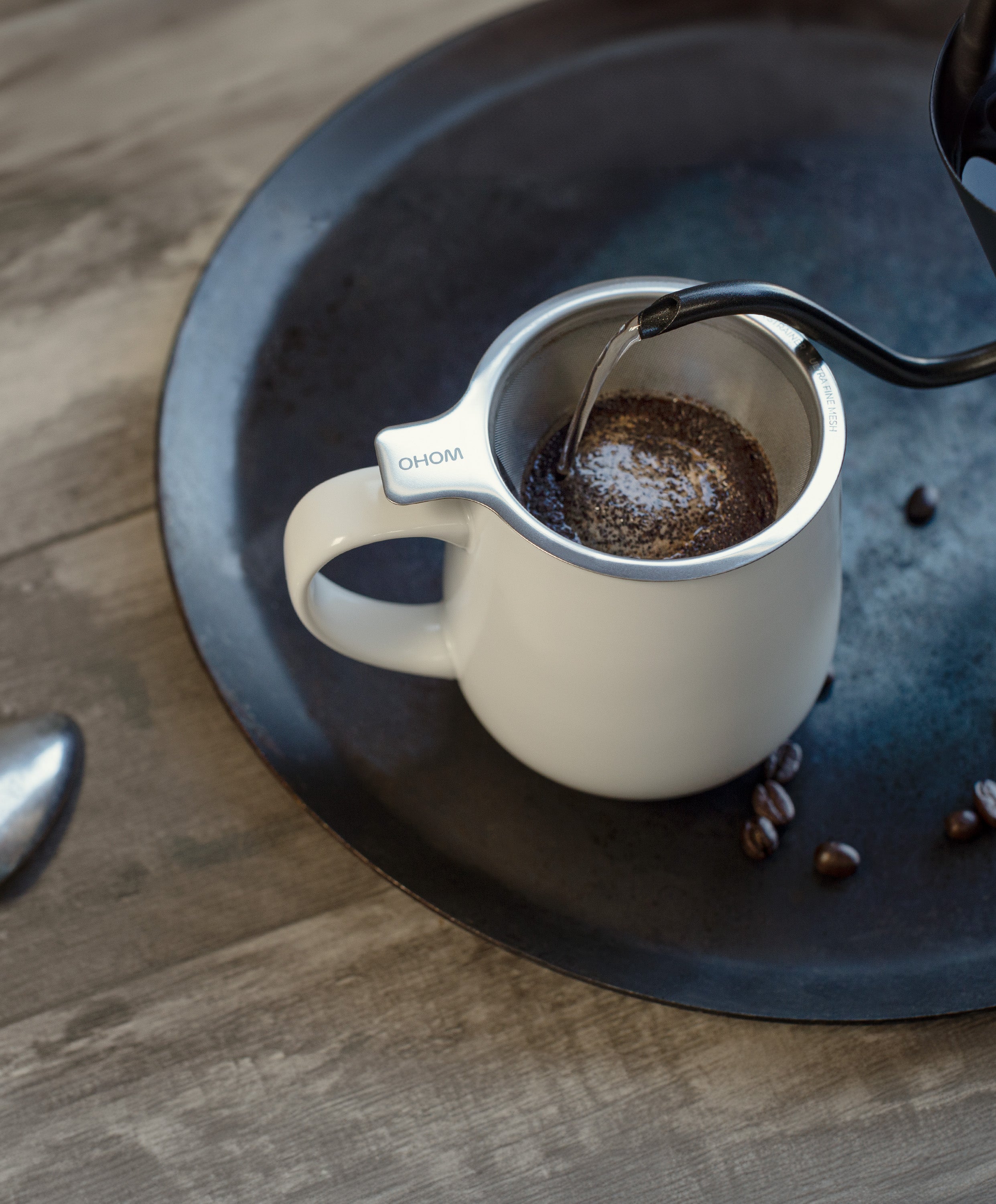 Hot water being poured into Ui large stainless steel strainer in Ui 2 / Ui 3 self-heating ceramic mug 12 fl oz, ground coffee in strainer and coffee beans beside mug