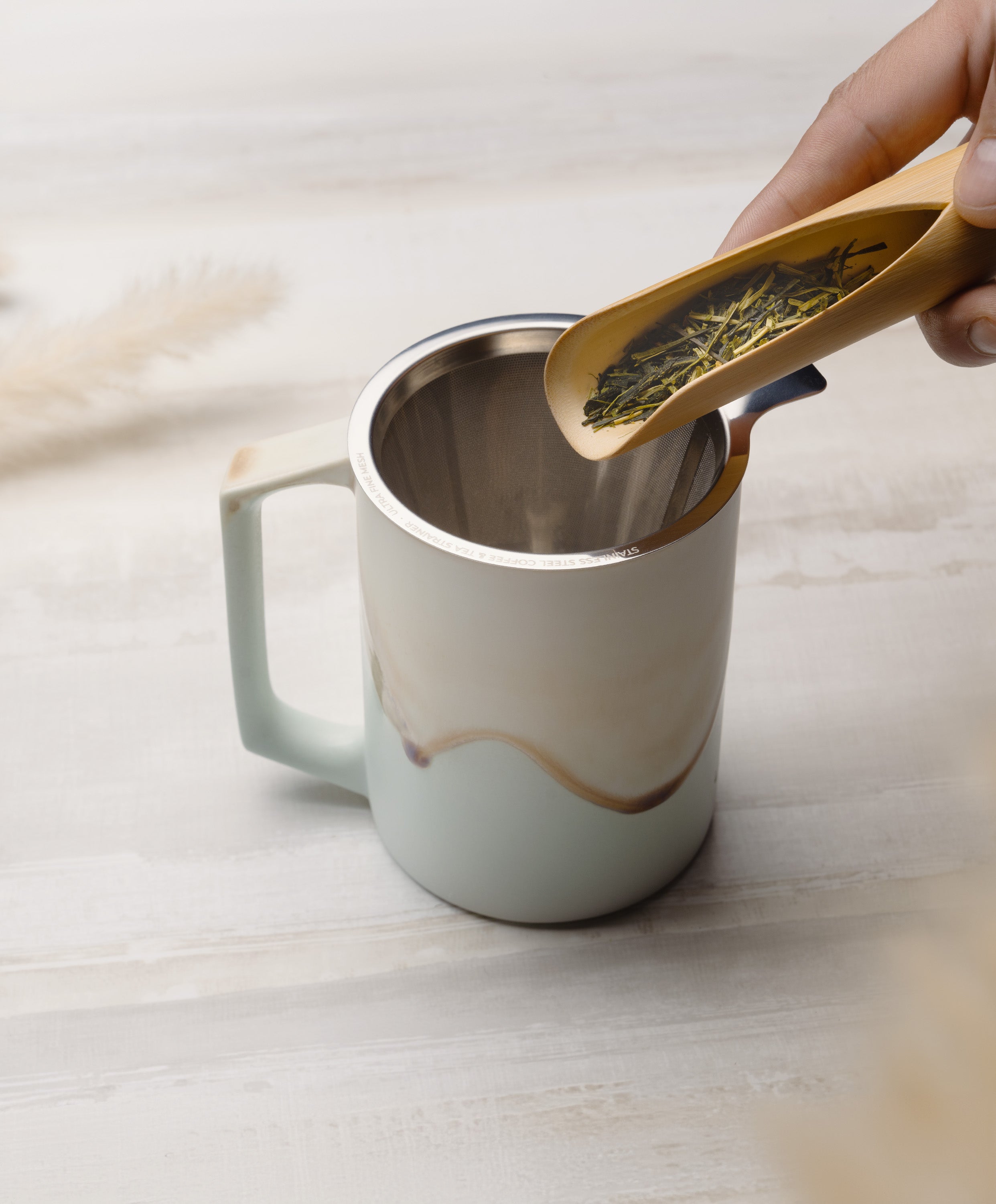 Ui large stainless steel strainer in Ui Artist Collection Mug set Mint Glacier, person about to pour tea into strainer for brewing