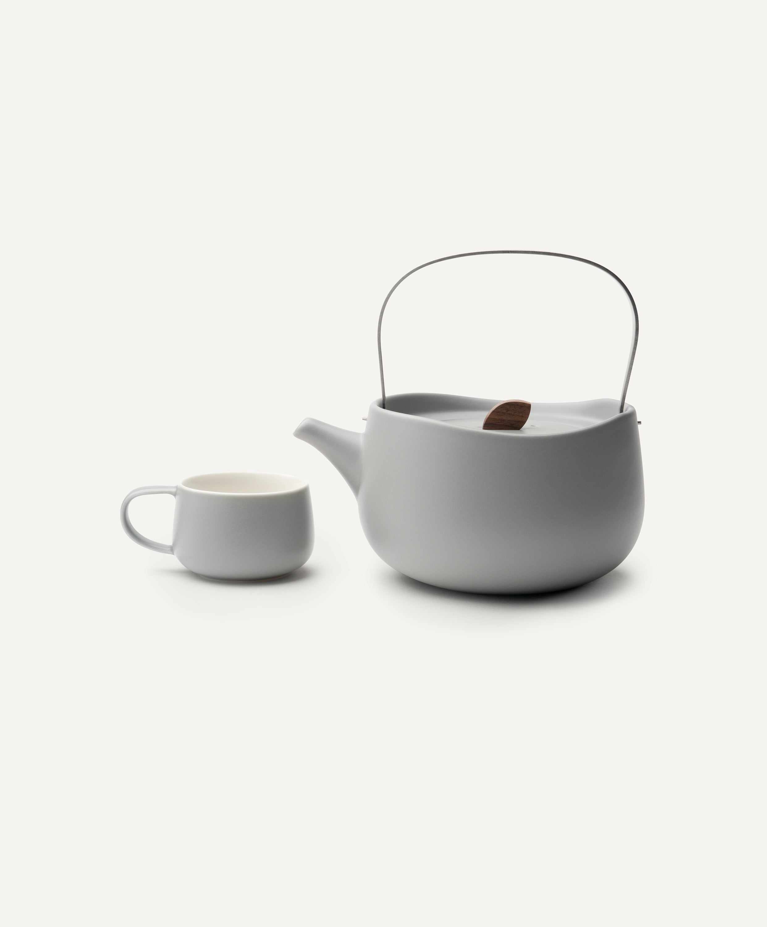 Leiph self-heating ceramic teapot 20 fl oz / 600 mL in Soft Gray with lid on top and matching teacups next to it