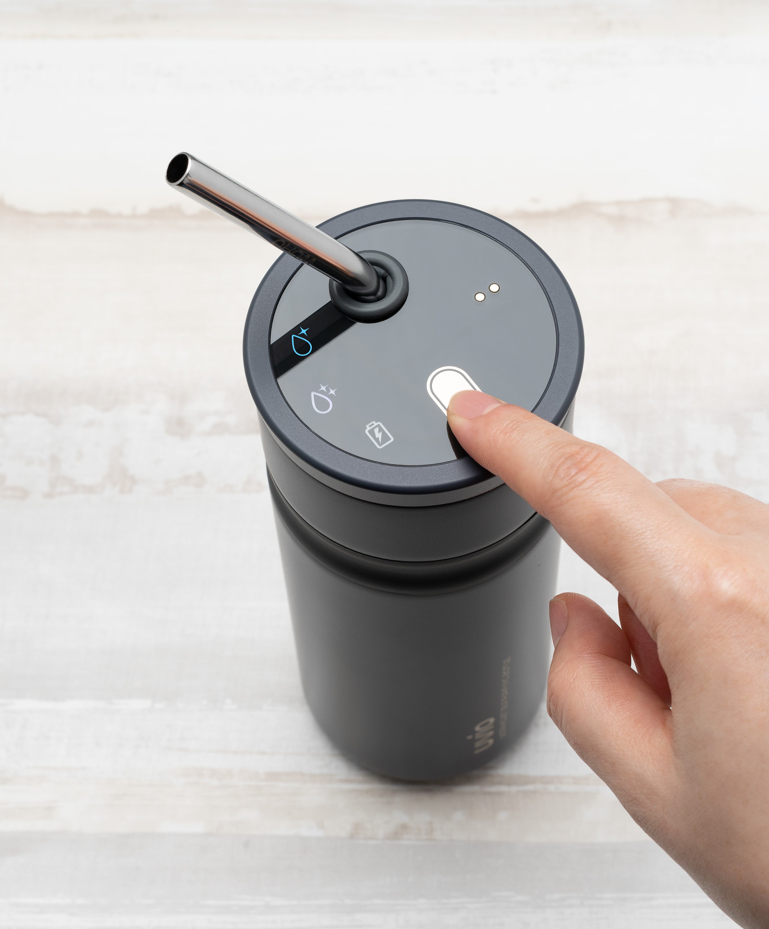 Person pressing button on Uvio self-purifying water bottle 16 fl oz / 480 mL in Charcoal Black to activate UV-C purification