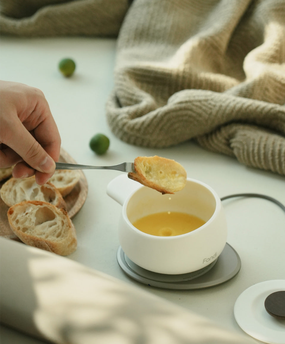 Person dipping bread into Fondi 7.6 fl oz / 225 mL self-heating ceramic fondue set with melted butter charging on OHOM Pad 3