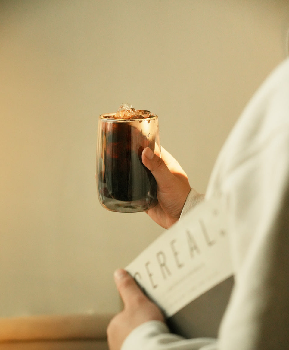 Person holding Sio dual-wall glass 8 fl oz / 236 mL filled with iced tea, made from fine quality borosilicate glass.