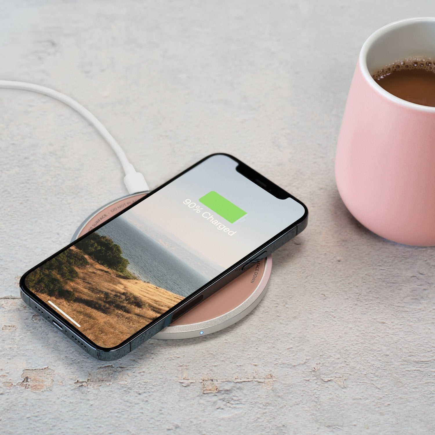 Pink mug with coffee next to phone on charging pad