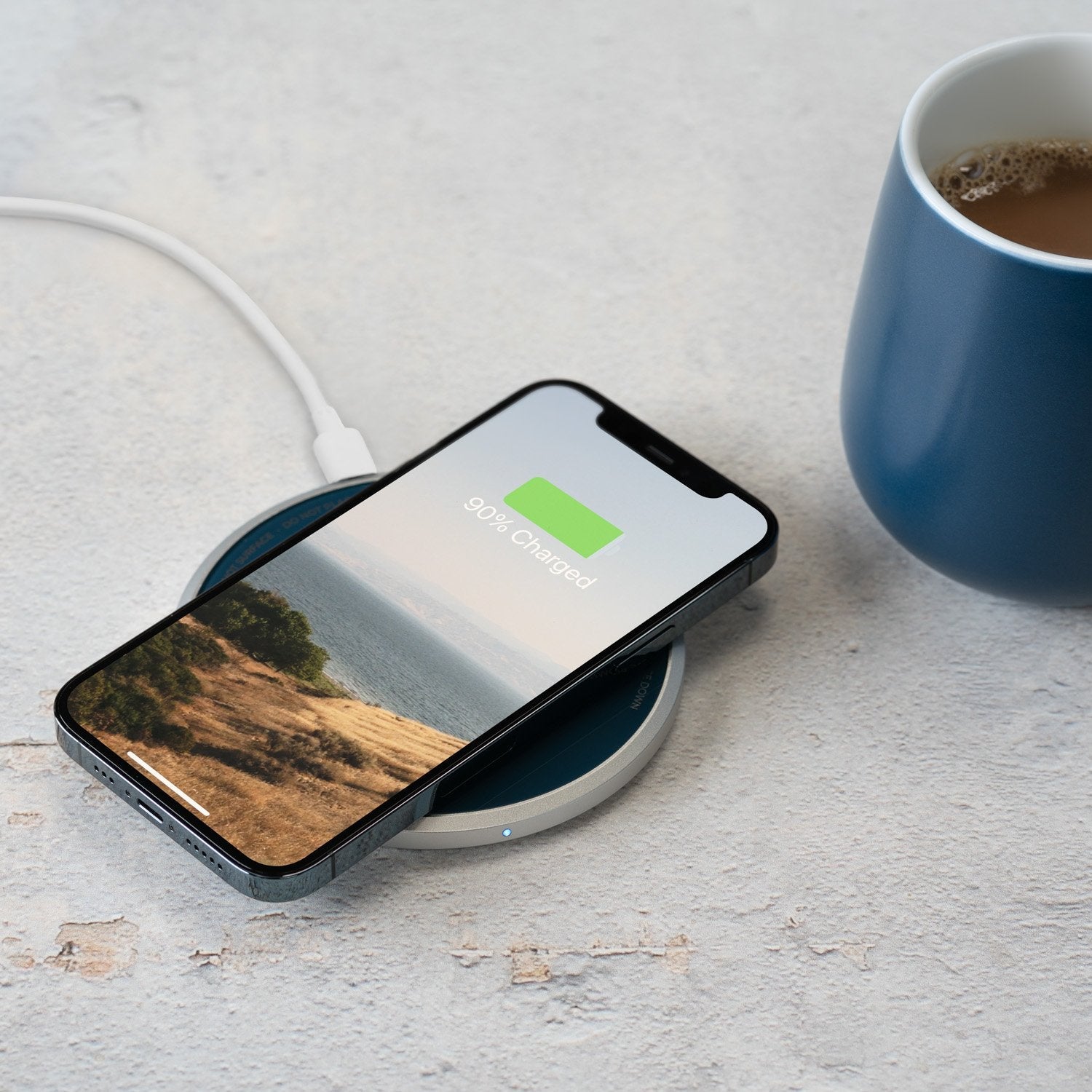 Navy mug with coffee next to phone on charging pad