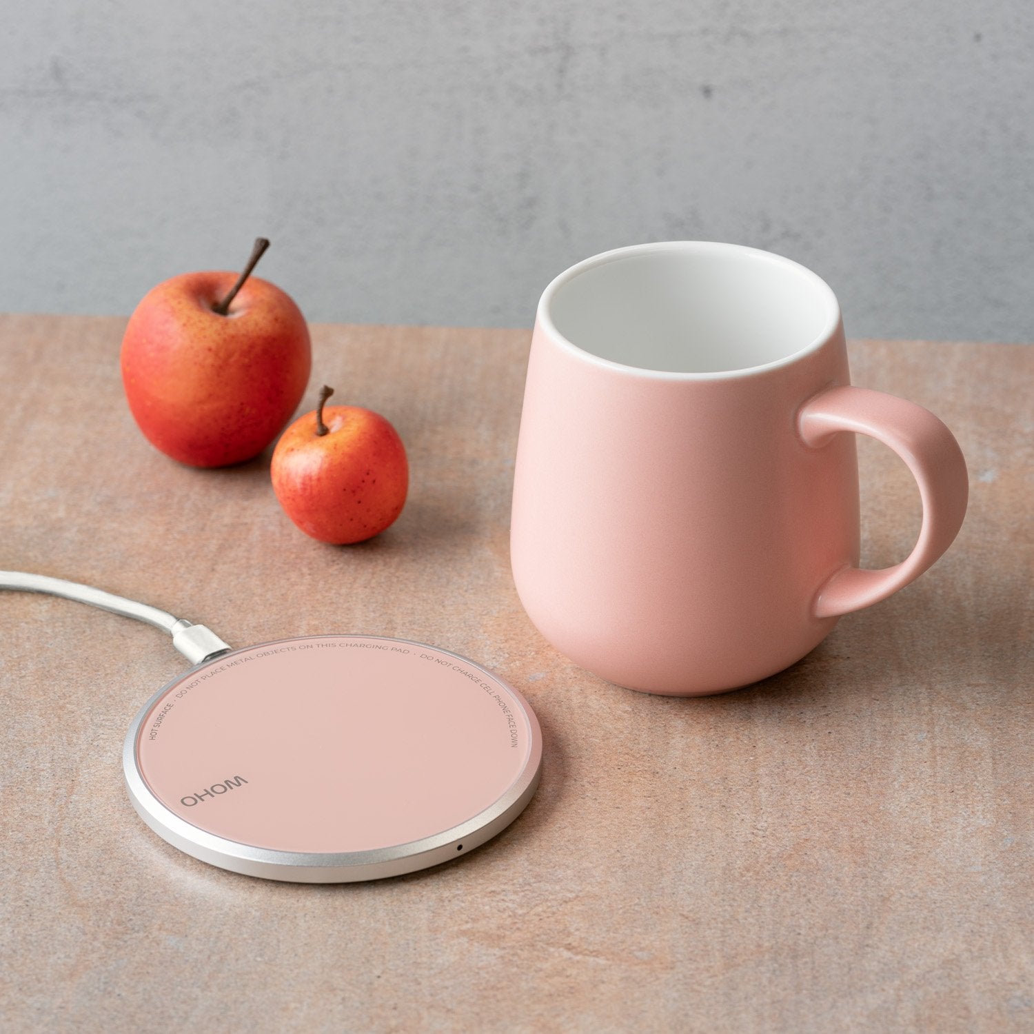 Pink mug next to heating pad with fruit on table