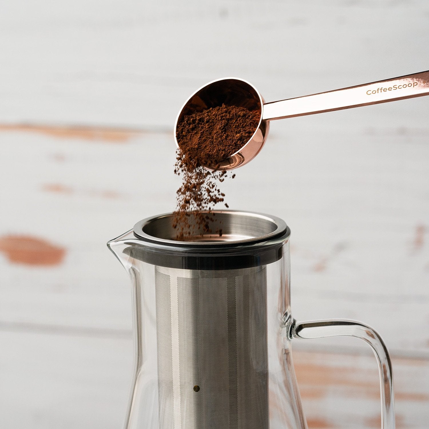 Copper colored coffee spoon pouring coffee grinds into infuser