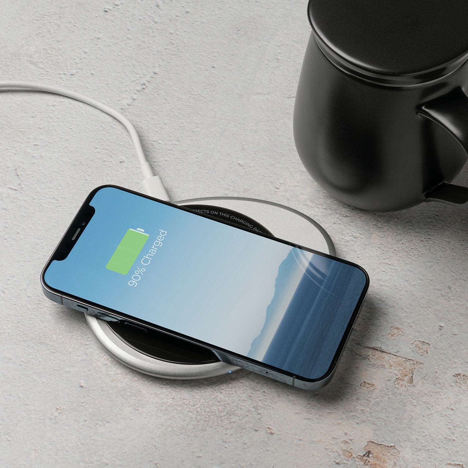 Black mug with lid next to phone on pebble charging pad