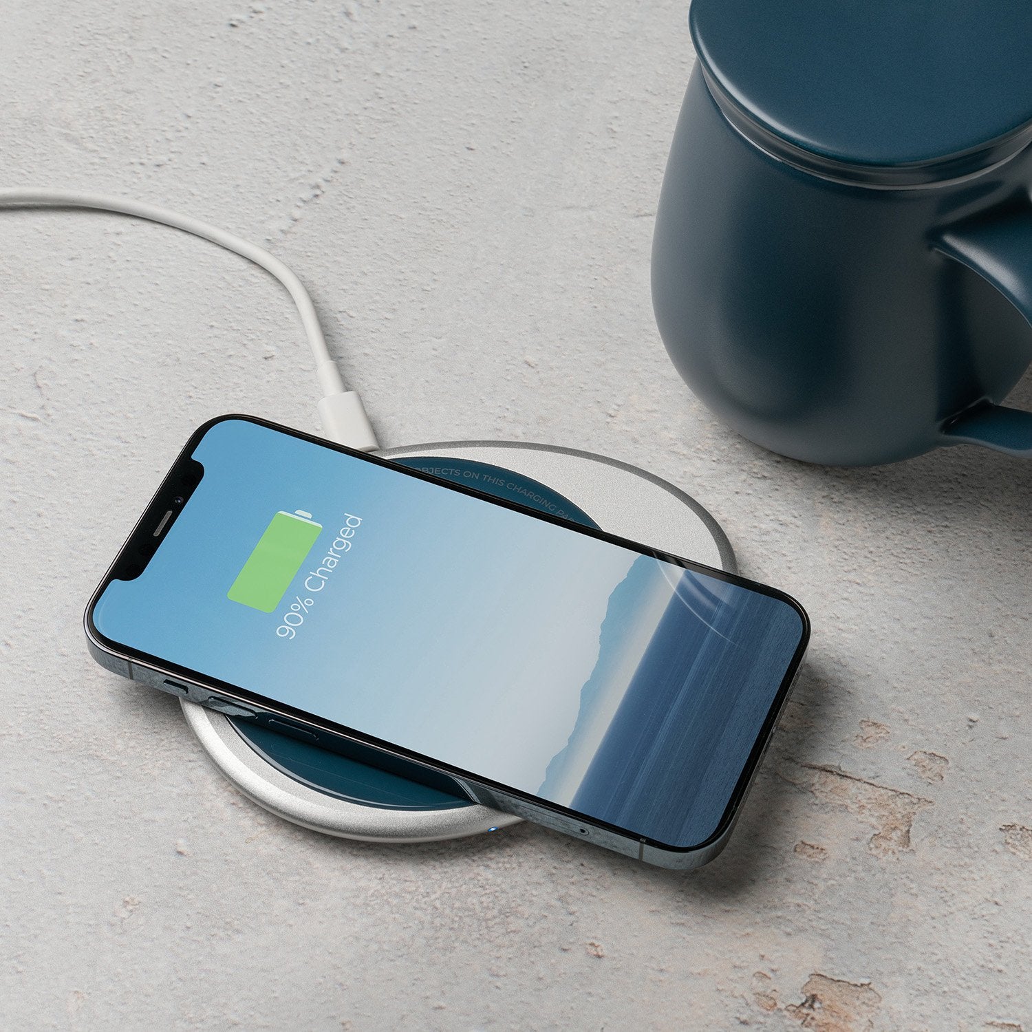 Navy mug with lid next to phone on navy pebble charging pad