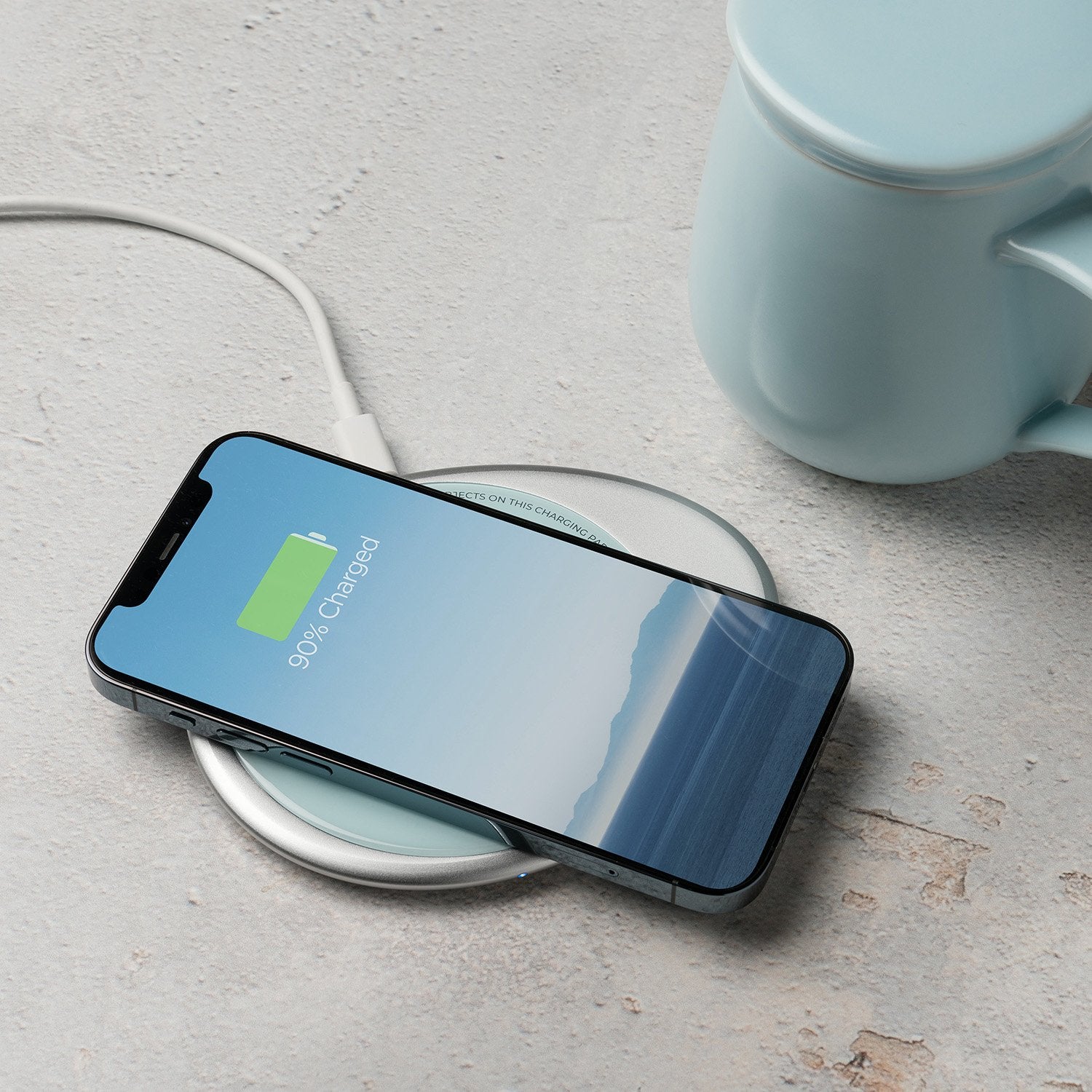 Light blue mug with lid next to phone on charging pad