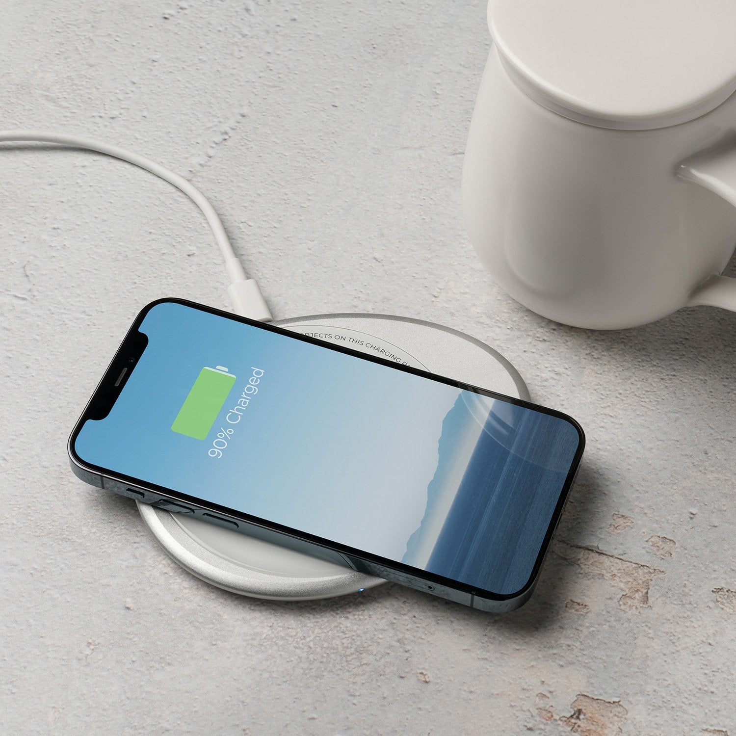 White mug with lid next to phone on white pebble charging pad