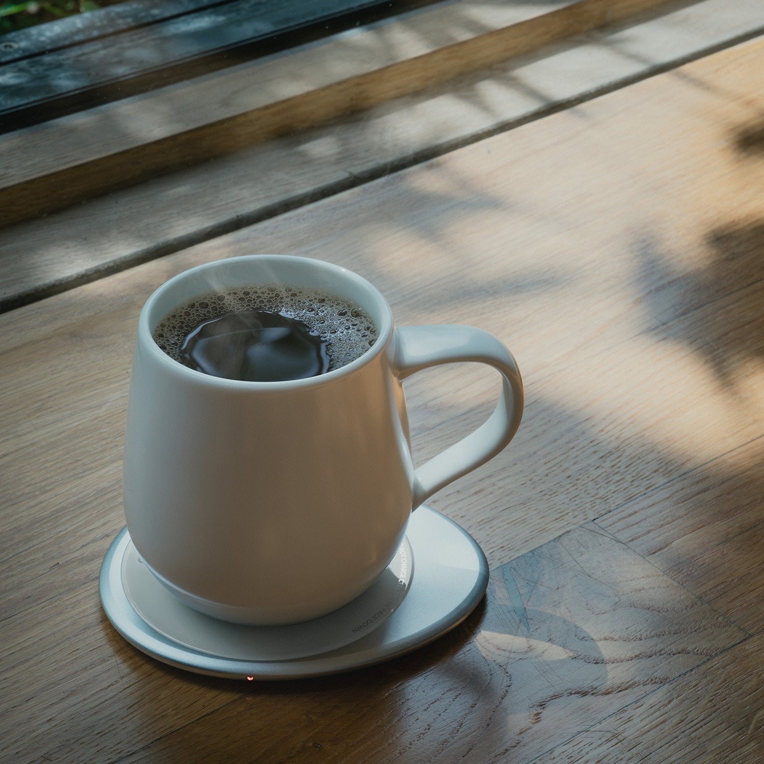 White mug with hot tea on heating pad on table