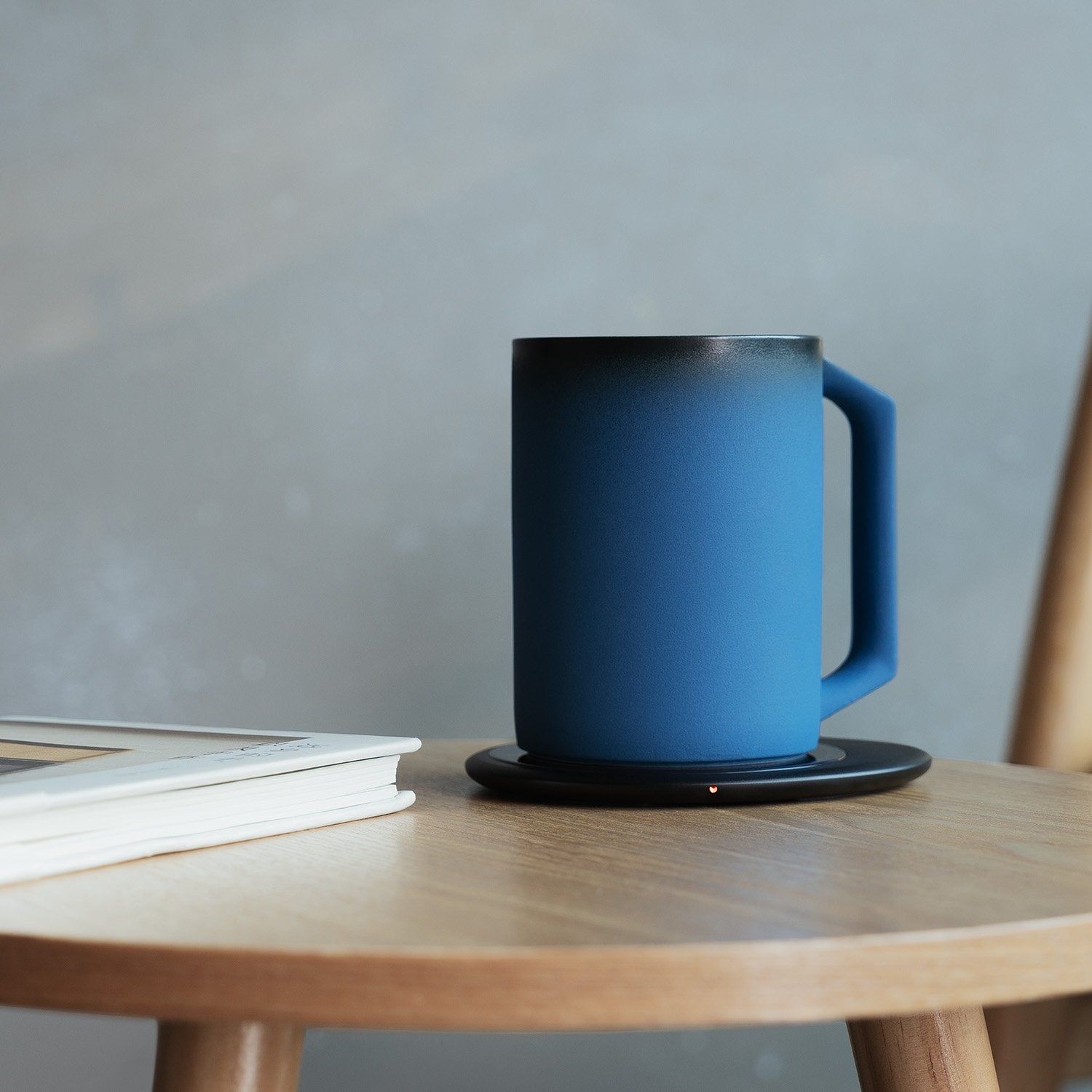 Dark blue mug on black pebble heating pad next to book